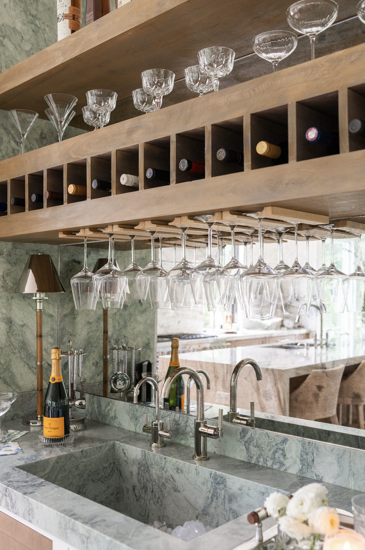 Interior of a bar with a marble countertop, hanging wine glasses, and a wooden shelf with various liquor bottles.