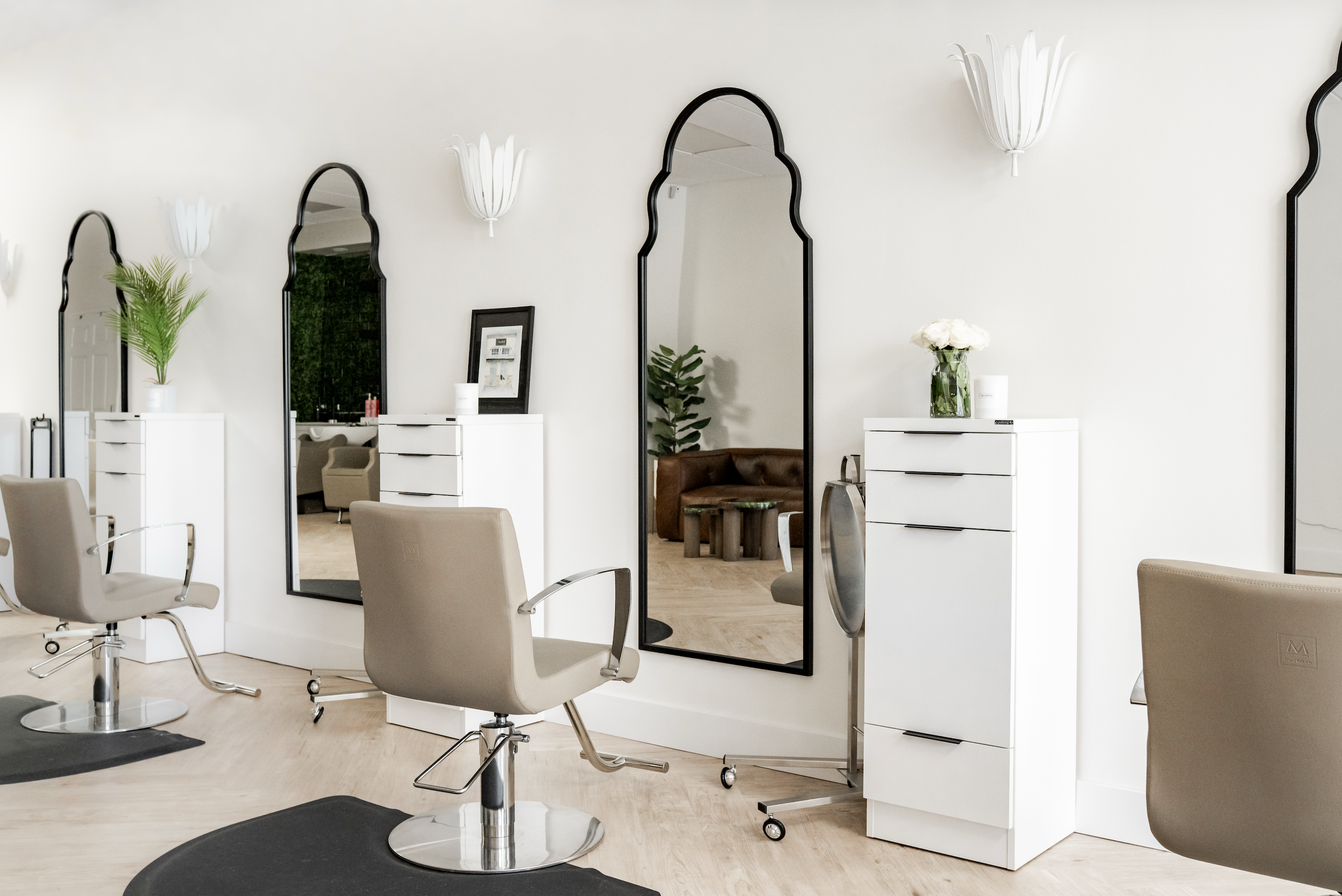 Salon chairs in front of mirrors with white cabinets, flowers, and plants in a hair salon.
