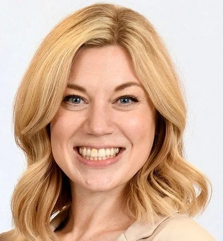 Close-up of a smiling woman with blonde hair and blue eyes against a plain background.