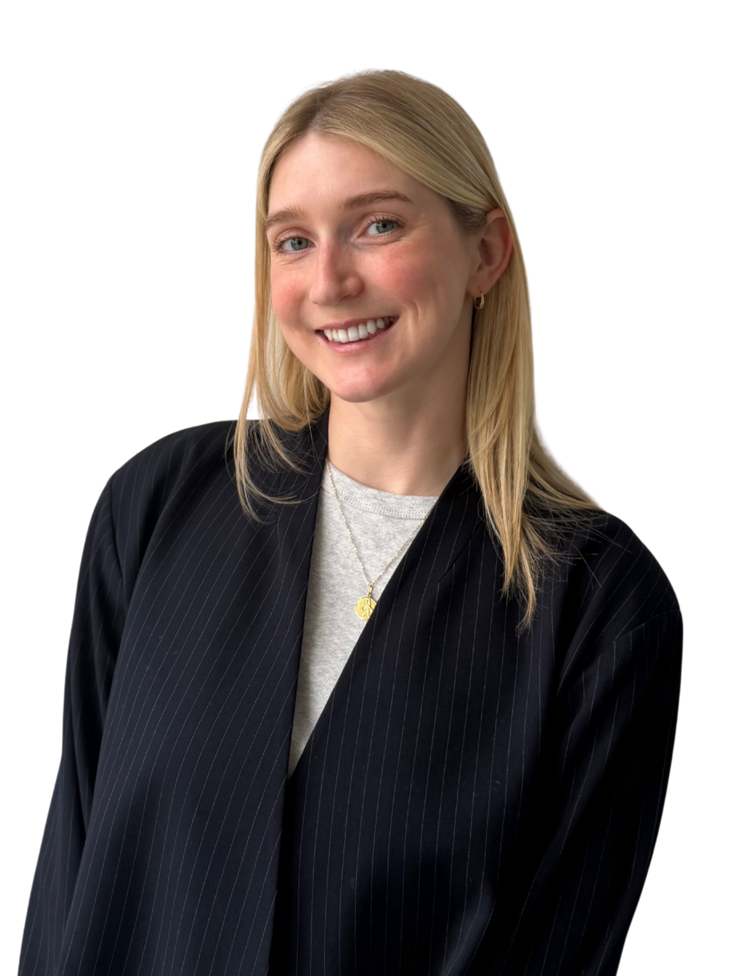 A woman with blonde hair and blue eyes smiling, dressed in a black pinstripe blazer, a grey top, and wearing gold hoop earrings and layered necklaces, against a plain white background.