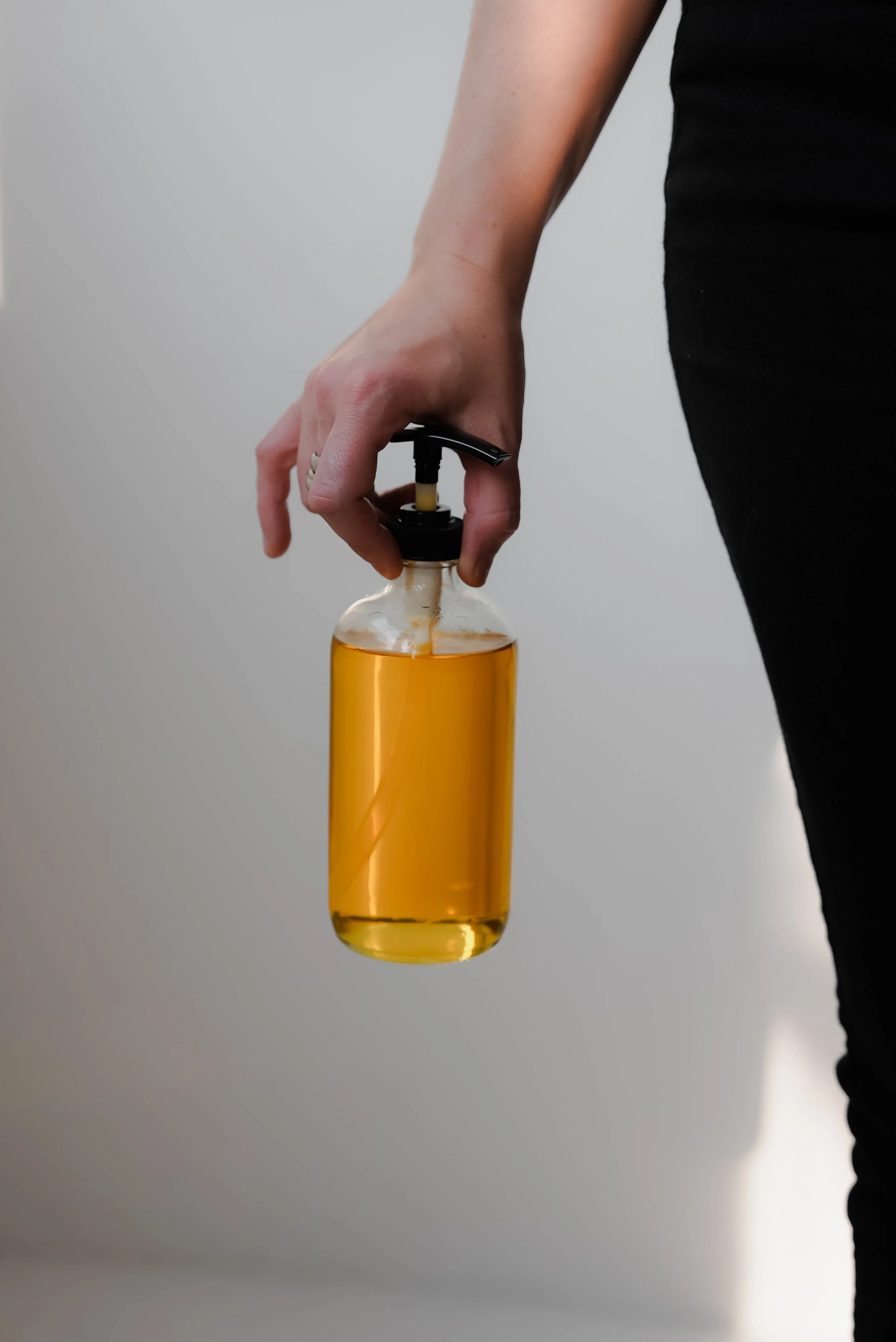 A person holding a clear glass bottle filled with yellow liquid, using a black pump dispenser.