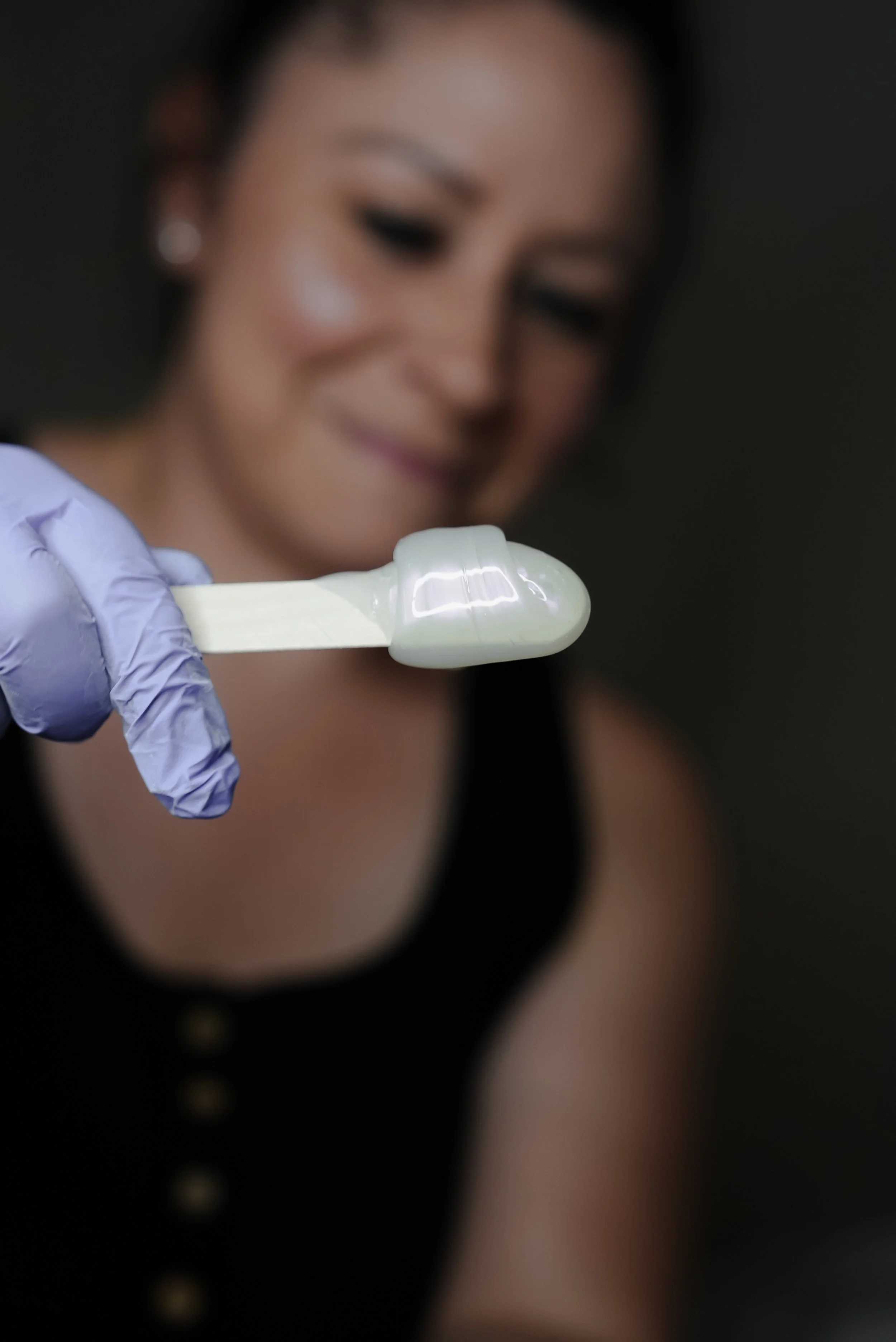 A woman smiling as she looks at a small, white, glossy object held with a purple gloved hand.