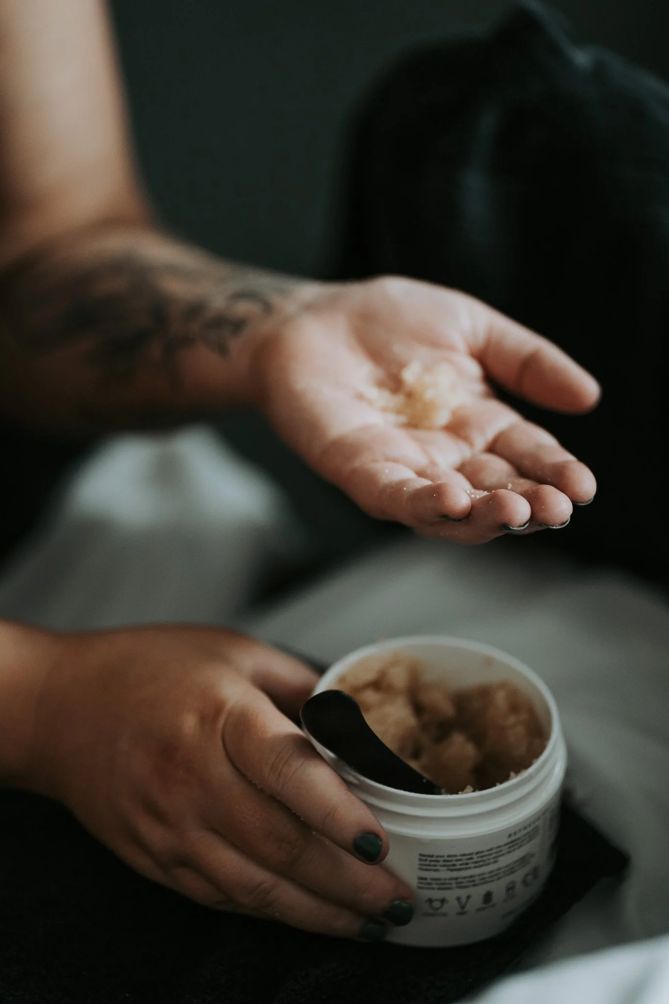 Close-up of a person opening a container of ice cream with a black spoon, sitting on a black surface.