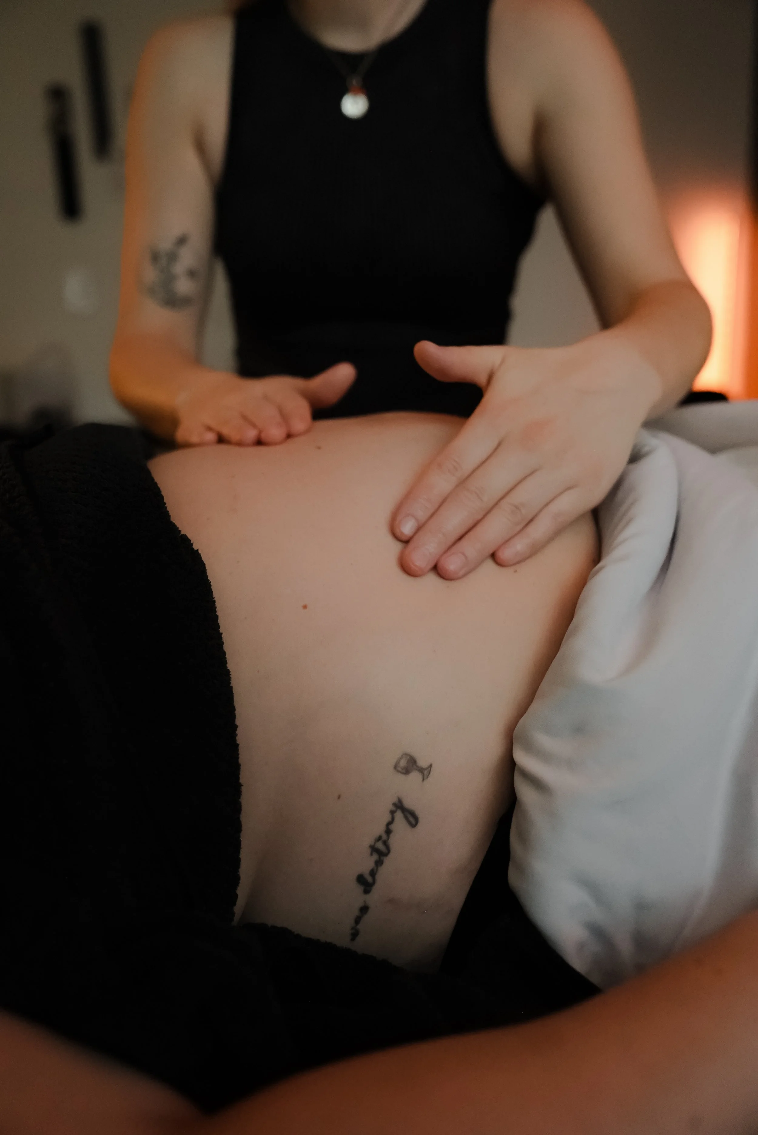 A person receiving a massage on their lower back with a tattoo that reads 'confidence' and a small wine glass icon.