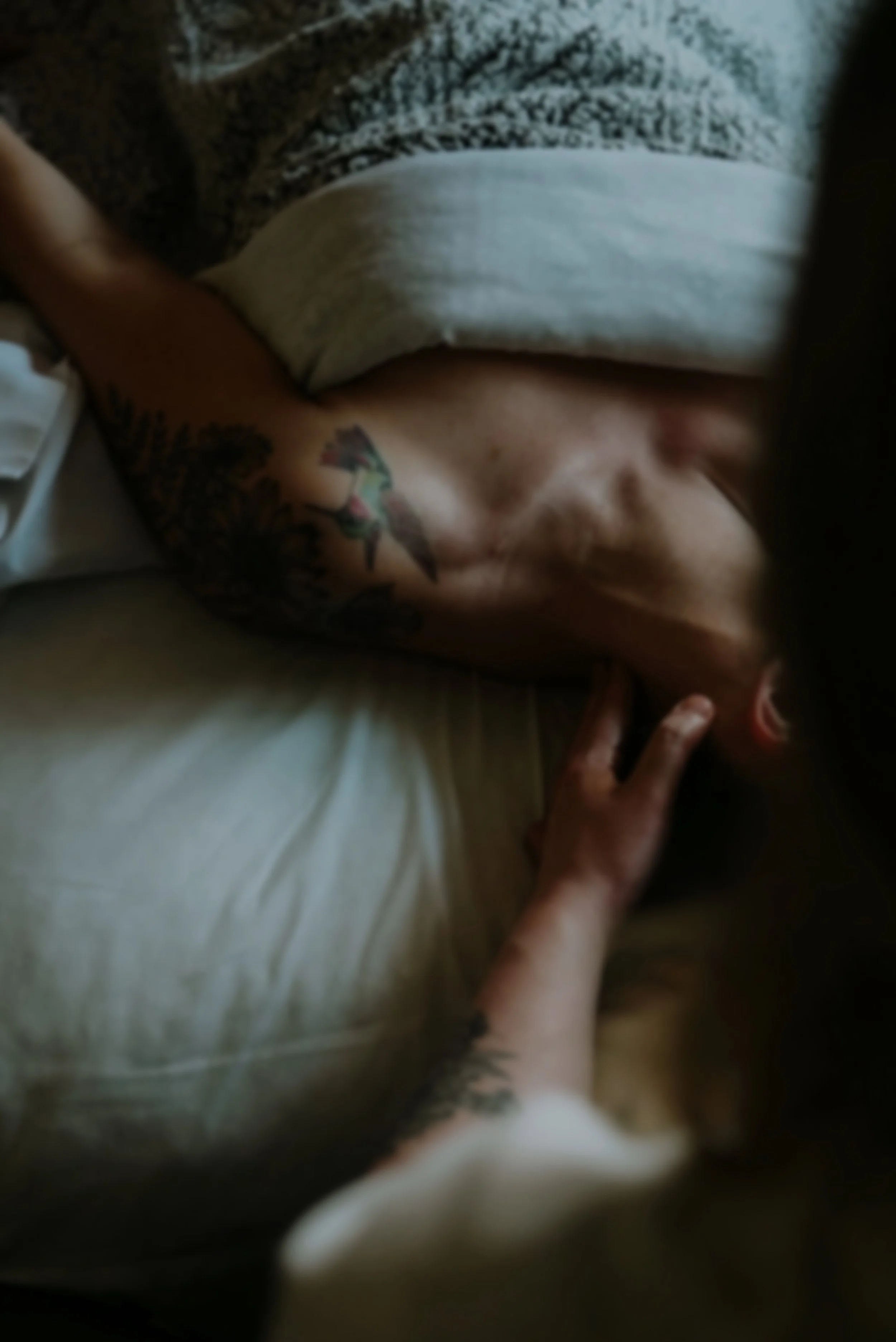 Close-up of a person lying down with visible tattoos on their arm, wearing a white shirt, and resting on a light-colored surface.