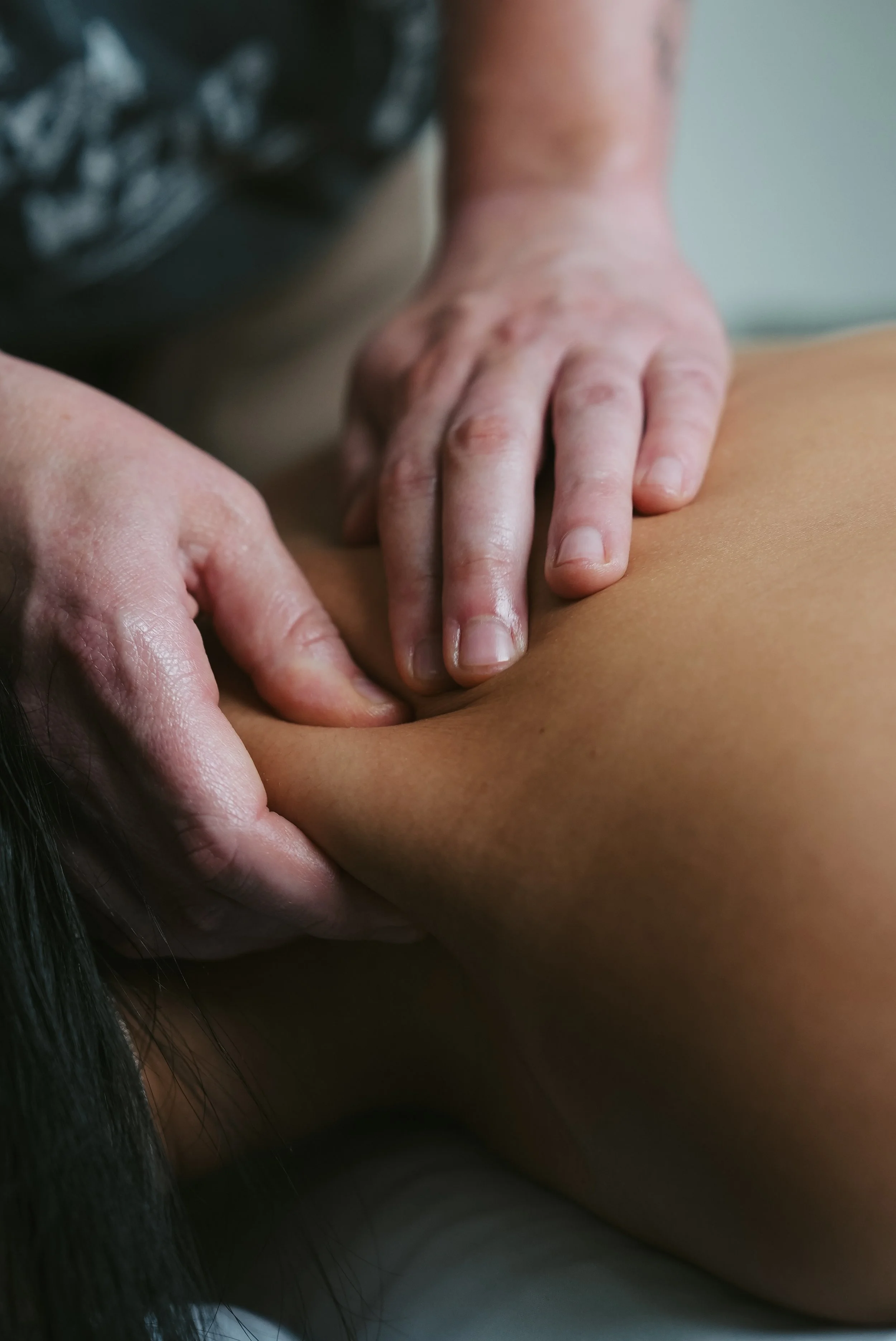 Close-up of a person receiving a back massage, showing the person's arm and a masseuse's hands applying pressure to the person's back.