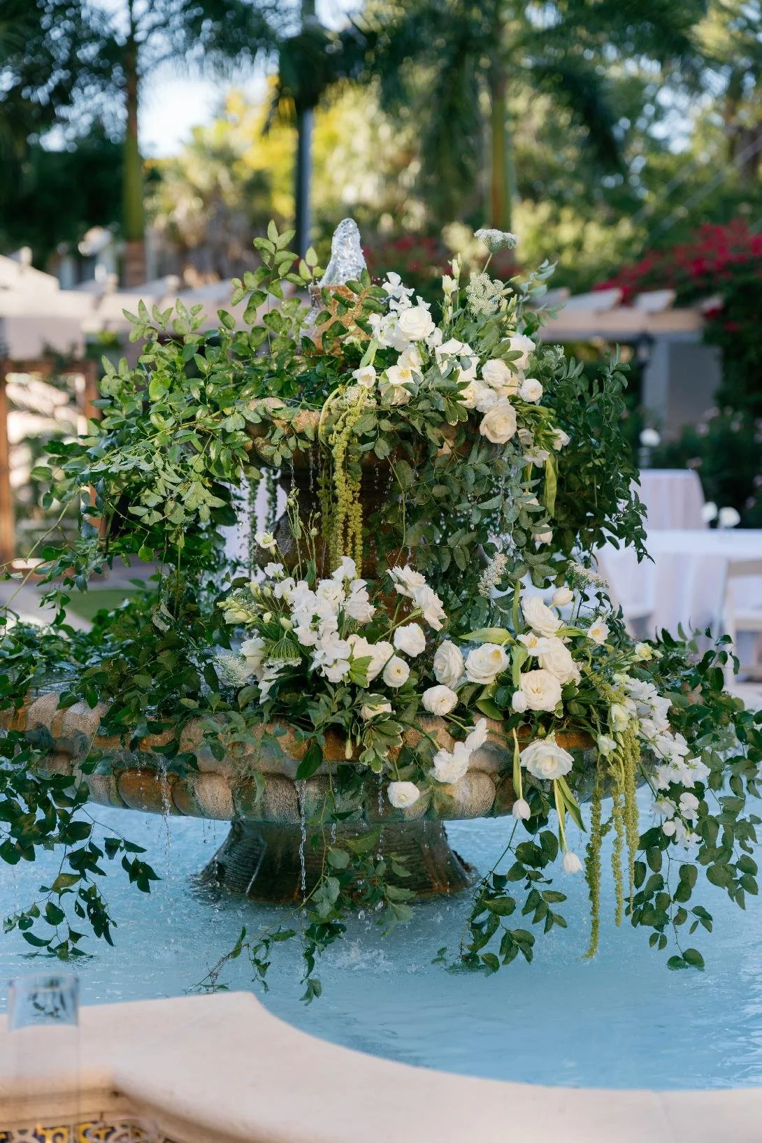 Elegant outdoor floral arrangement with white flowers and greenery in a tiered fountain.