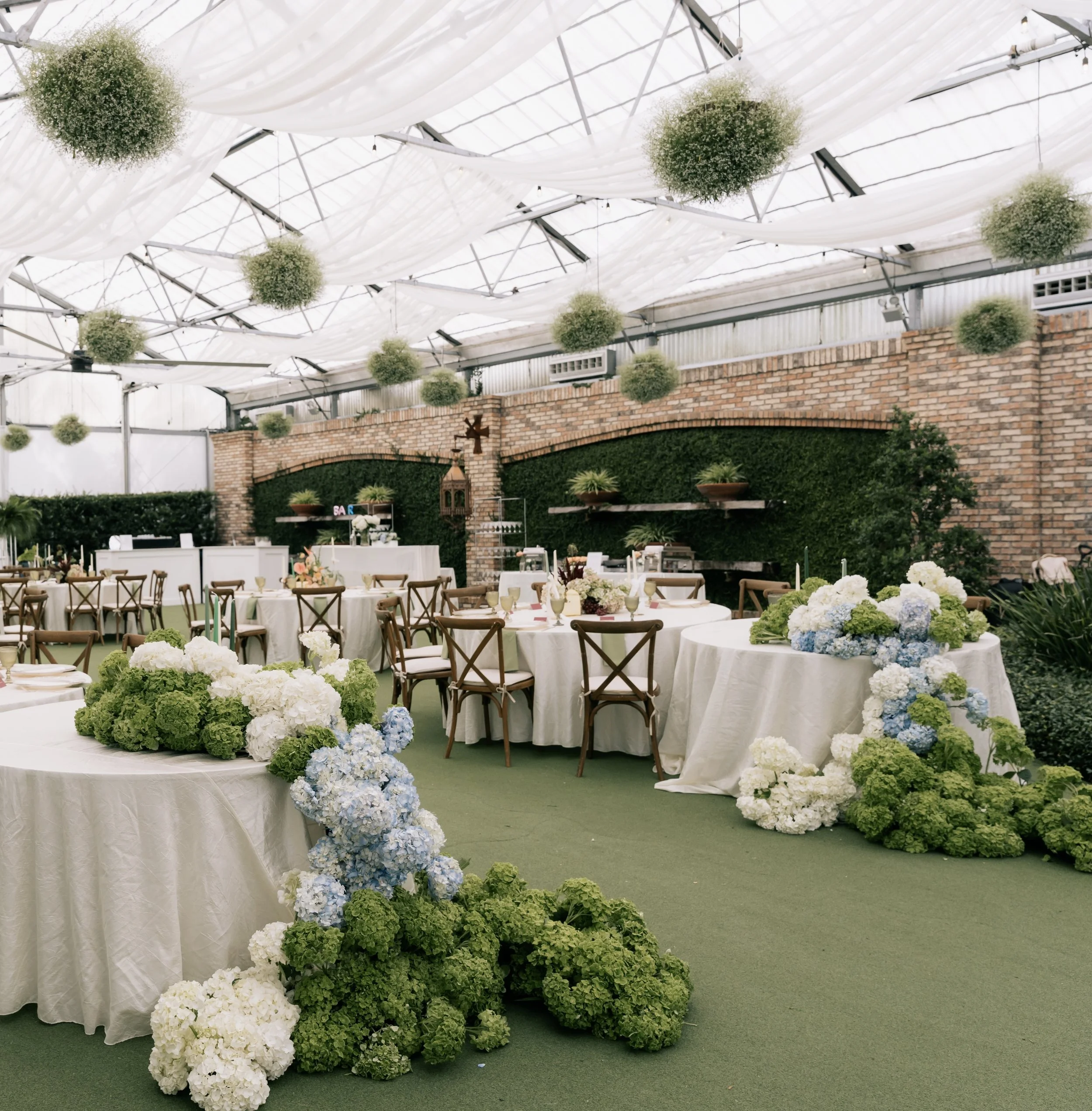Indoor event space decorated with white drapes, hanging round flower arrangements, and floral arrangements on tables and the floor.
