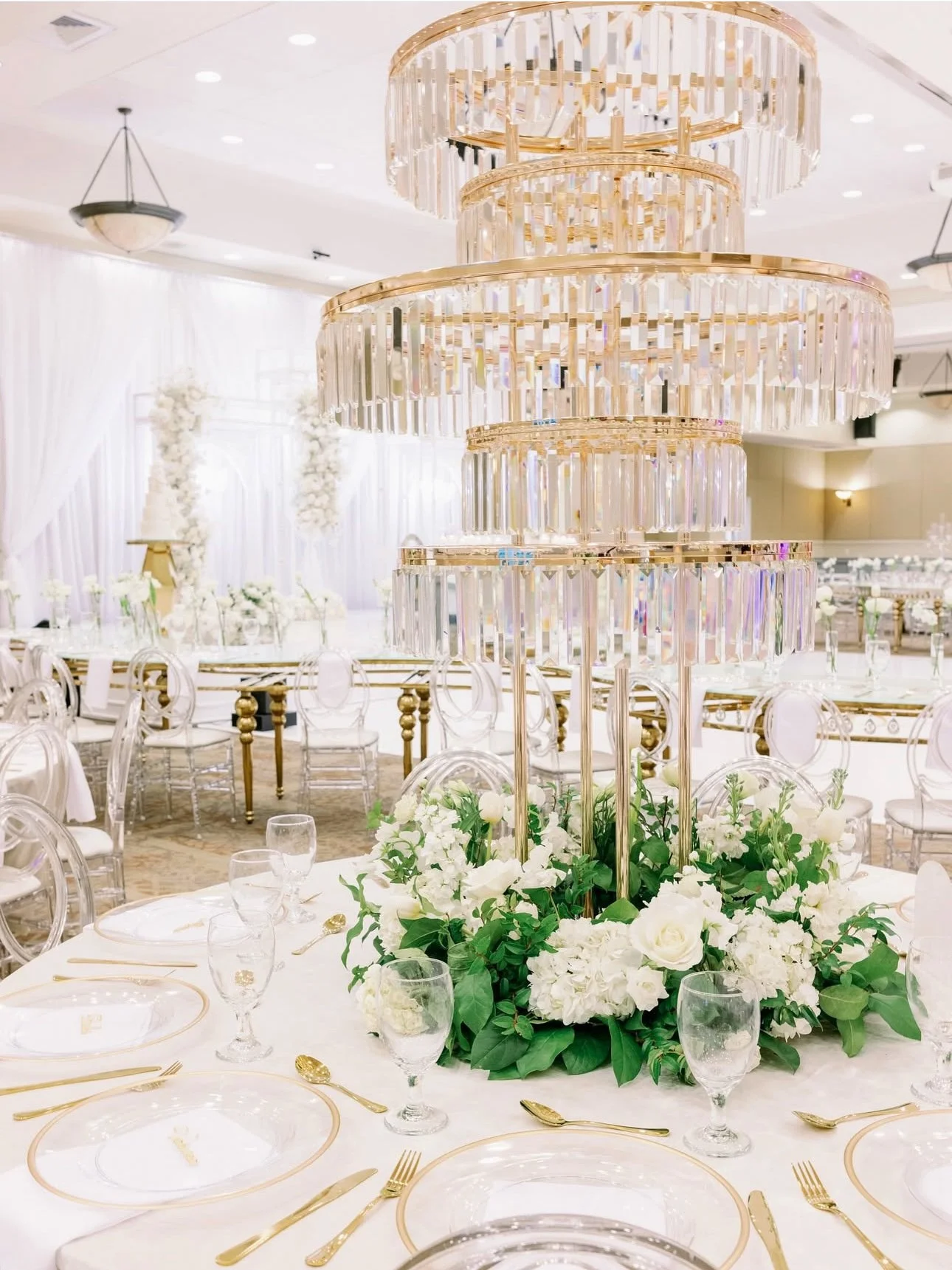 Elegant reception hall decorated with white drapes, floral arrangements, and a tiered crystal chandelier.