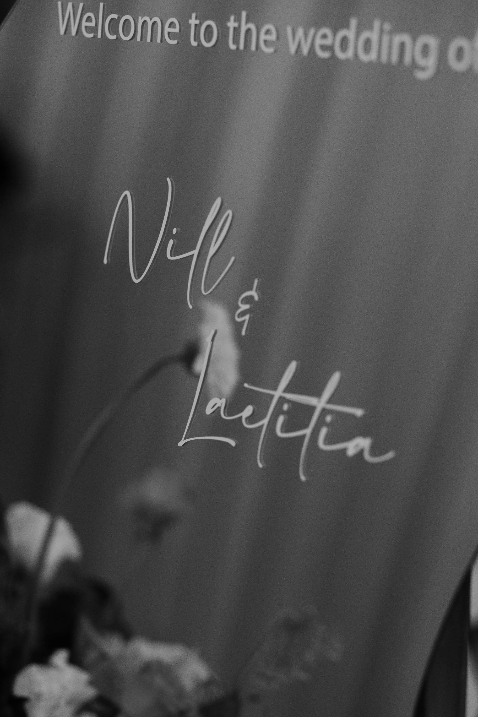 Close-up of a sign with the text 'Welcome to the wedding of' and the names 'Nill & Laitia' in cursive font.