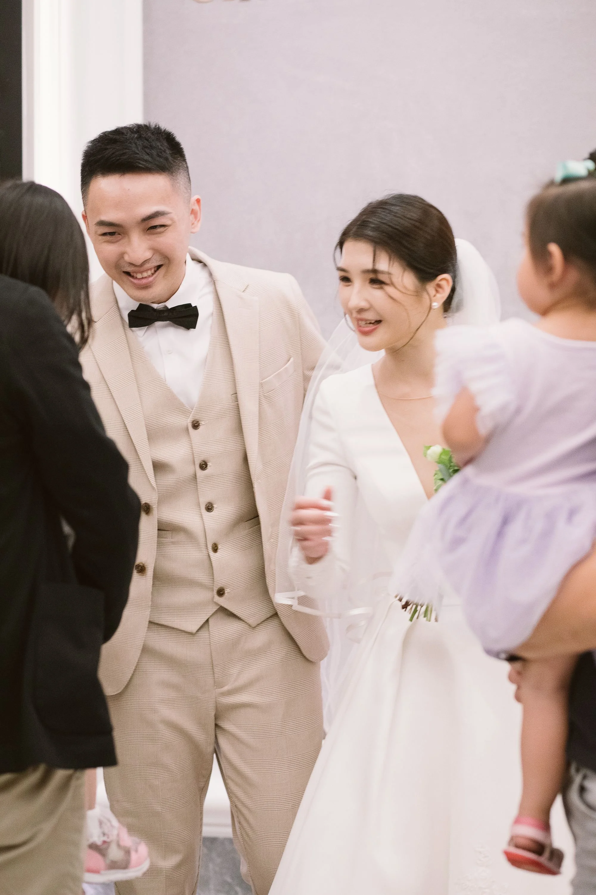 A newlywed couple in wedding attire smiling and talking with children at a celebration or gathering.