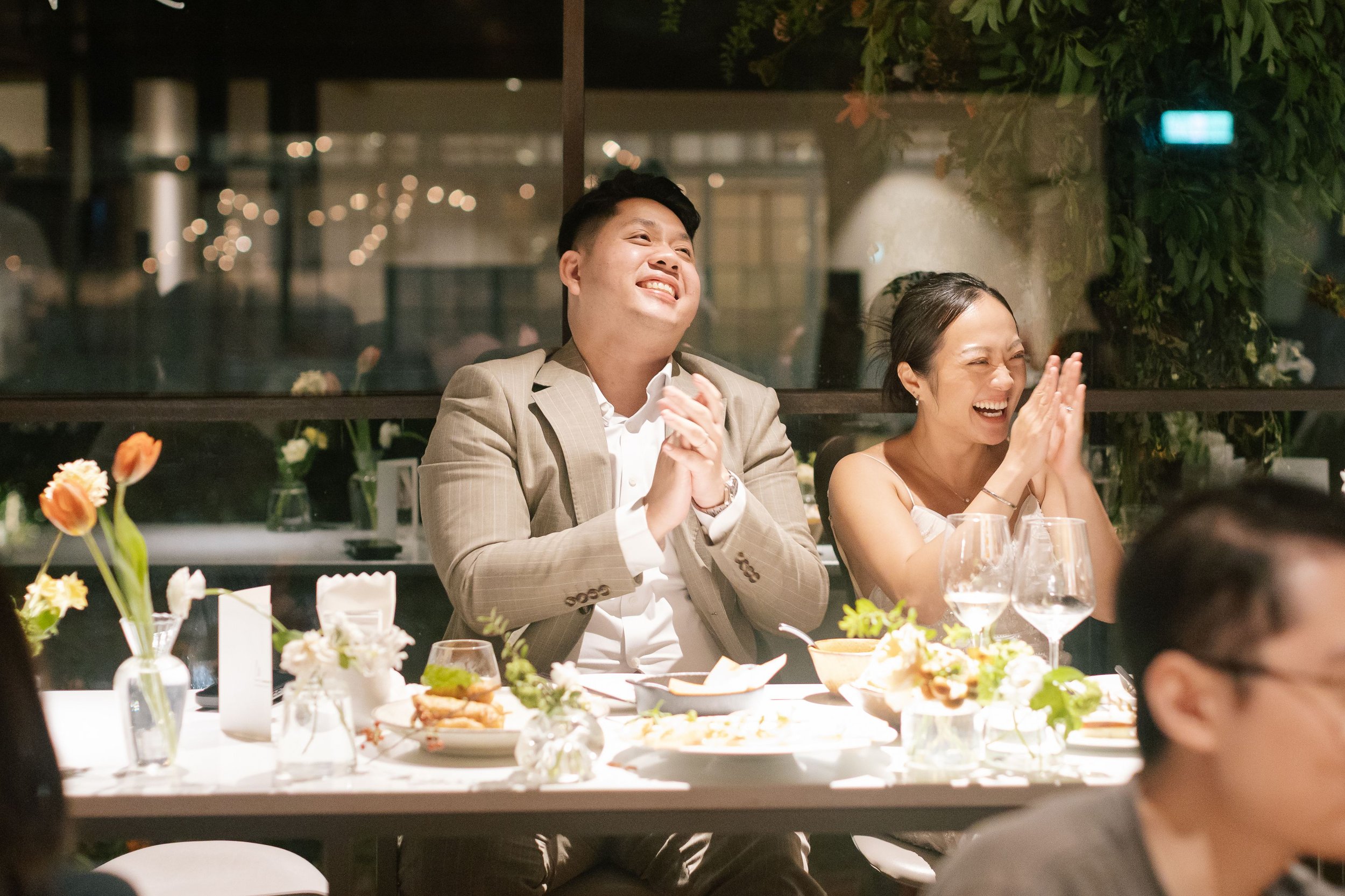 A man and woman seated at a banquet table, smiling and laughing during a celebration or dinner event at night.