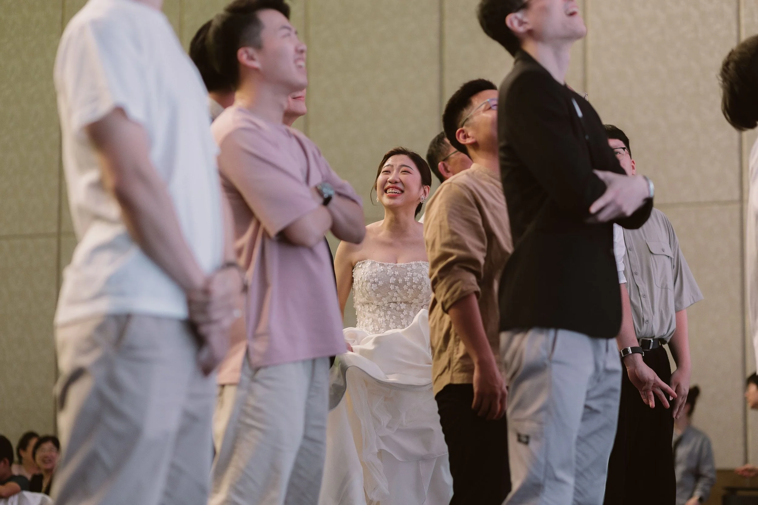A group of people standing in a line at a formal event, with the woman in a wedding gown at the center, smiling and laughing.