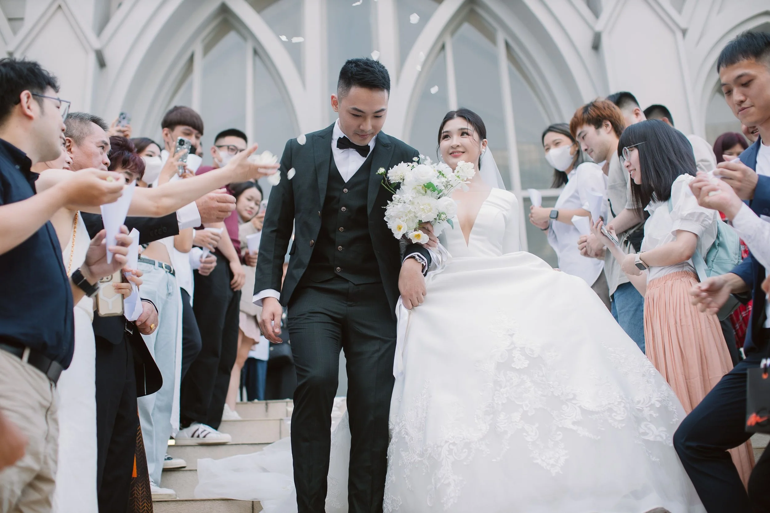A bride and groom ascending stairs surrounded by friends and family, celebrating their wedding.