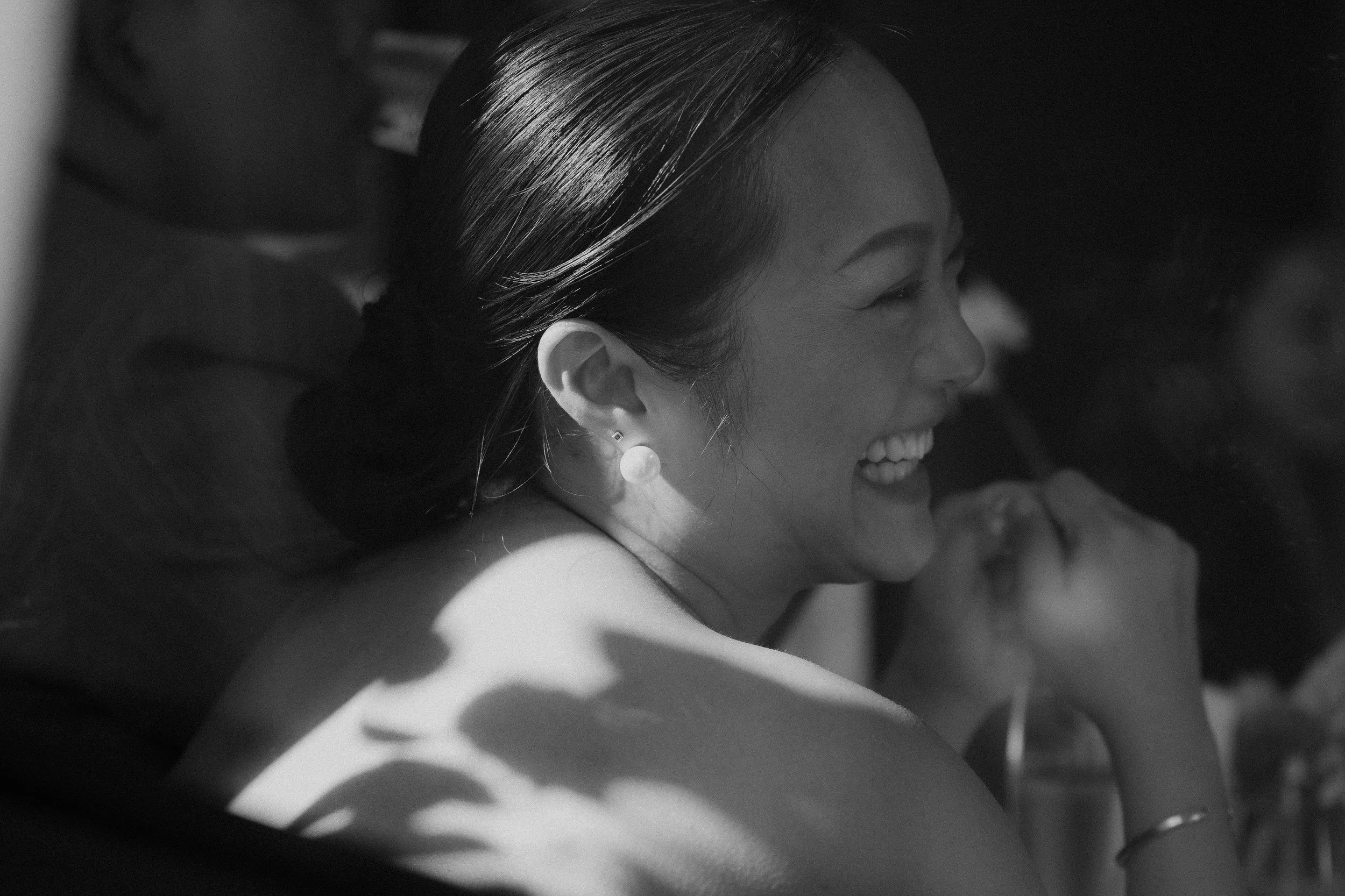 Close-up of a smiling woman with dark hair, wearing a pearl earring, in black and white.