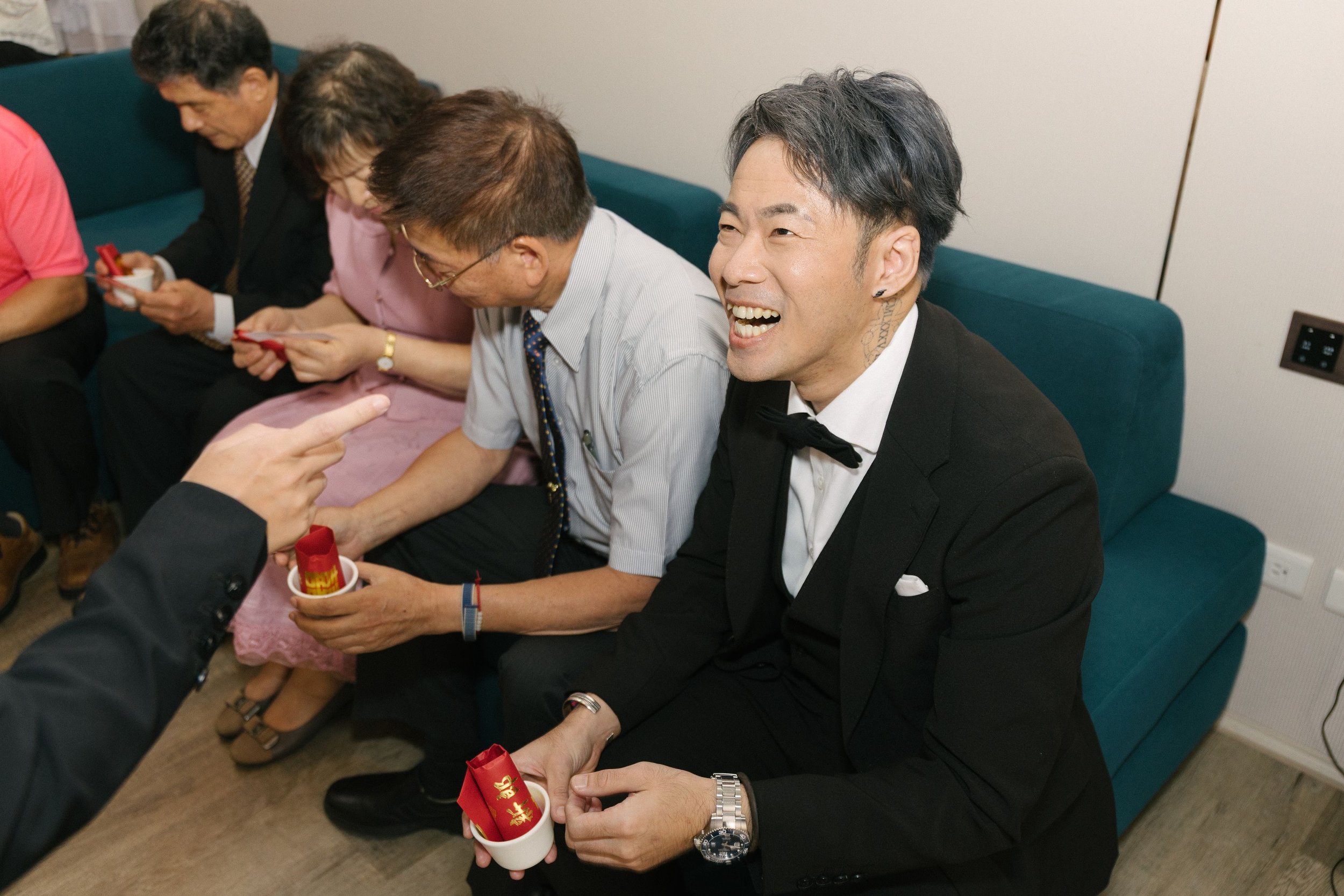 People sitting on a teal sofa, laughing and holding small cups with red and gold Chinese New Year decorations inside.