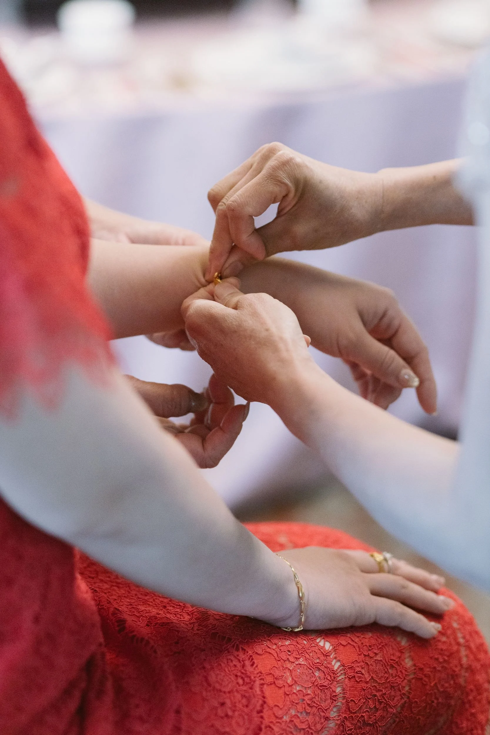 Close-up of a woman in red lace dress with silver bracelet, doing a traditional hand-held prayer or blessing with another person.