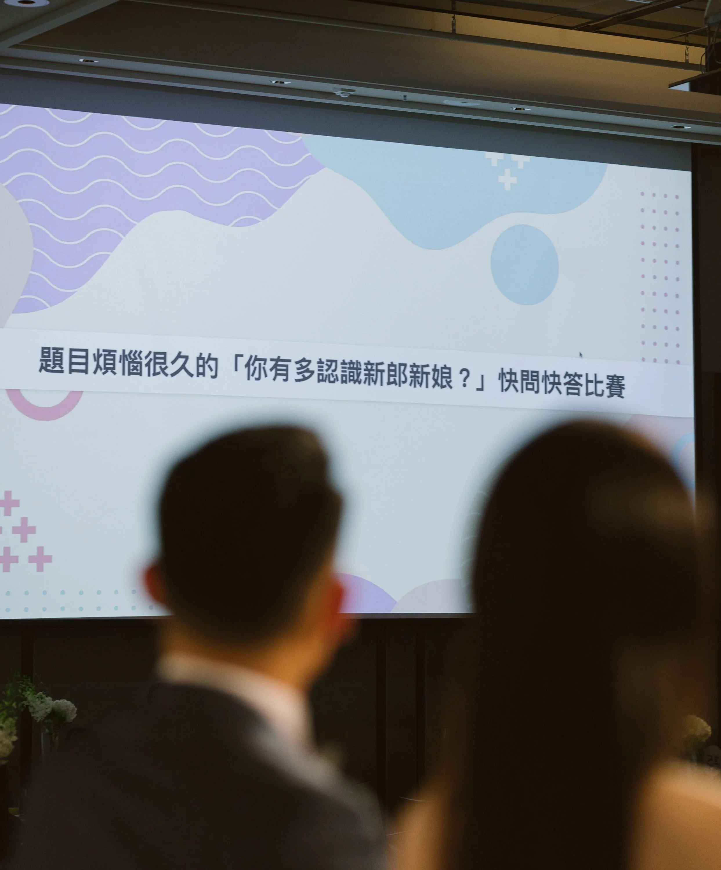 A presentation screen displaying text in Chinese characters and colorful, abstract background designs, with dark silhouettes of people in the foreground.