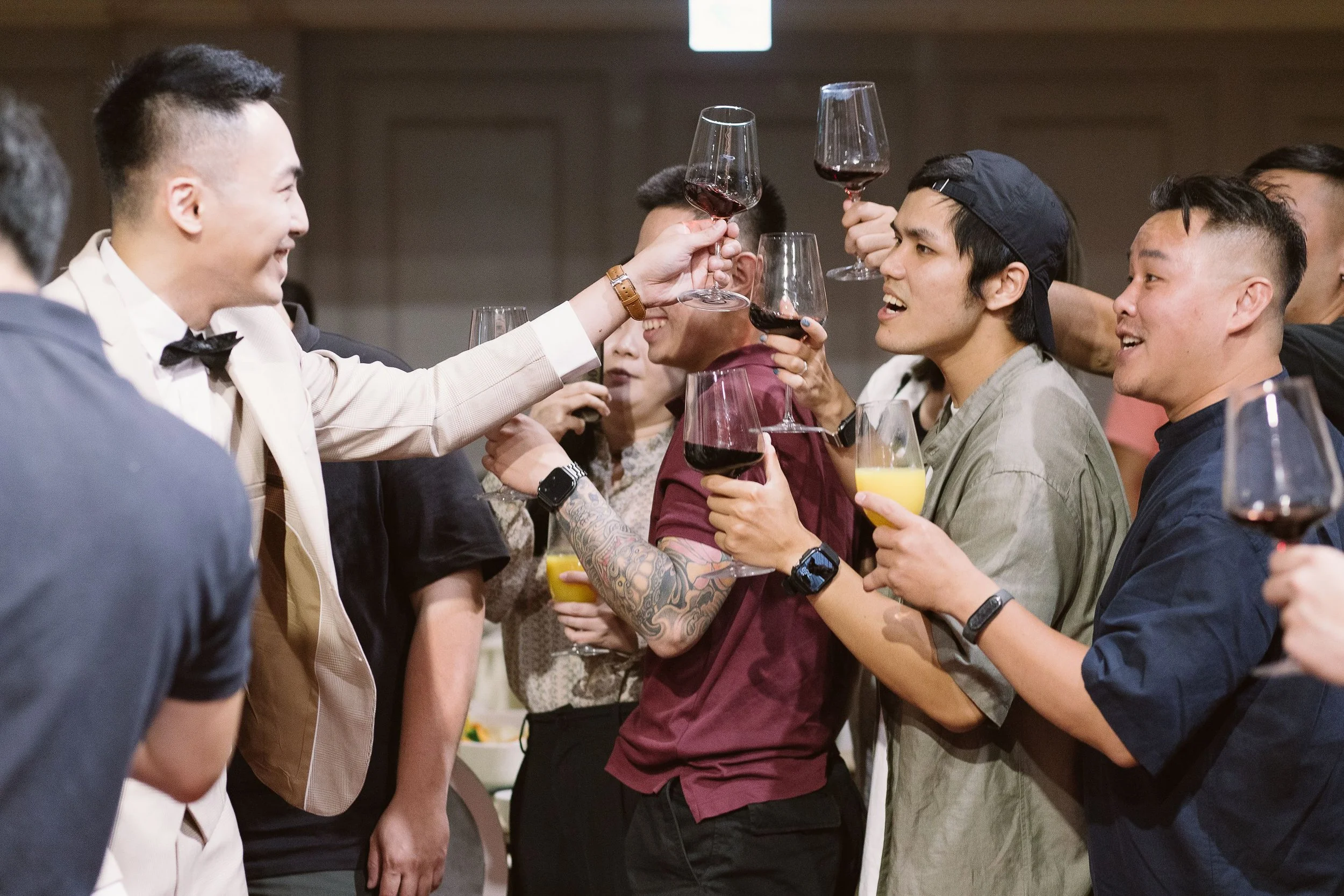 A group of people at a celebratory gathering toasting with glasses of red wine and orange juice, smiling and engaging with each other