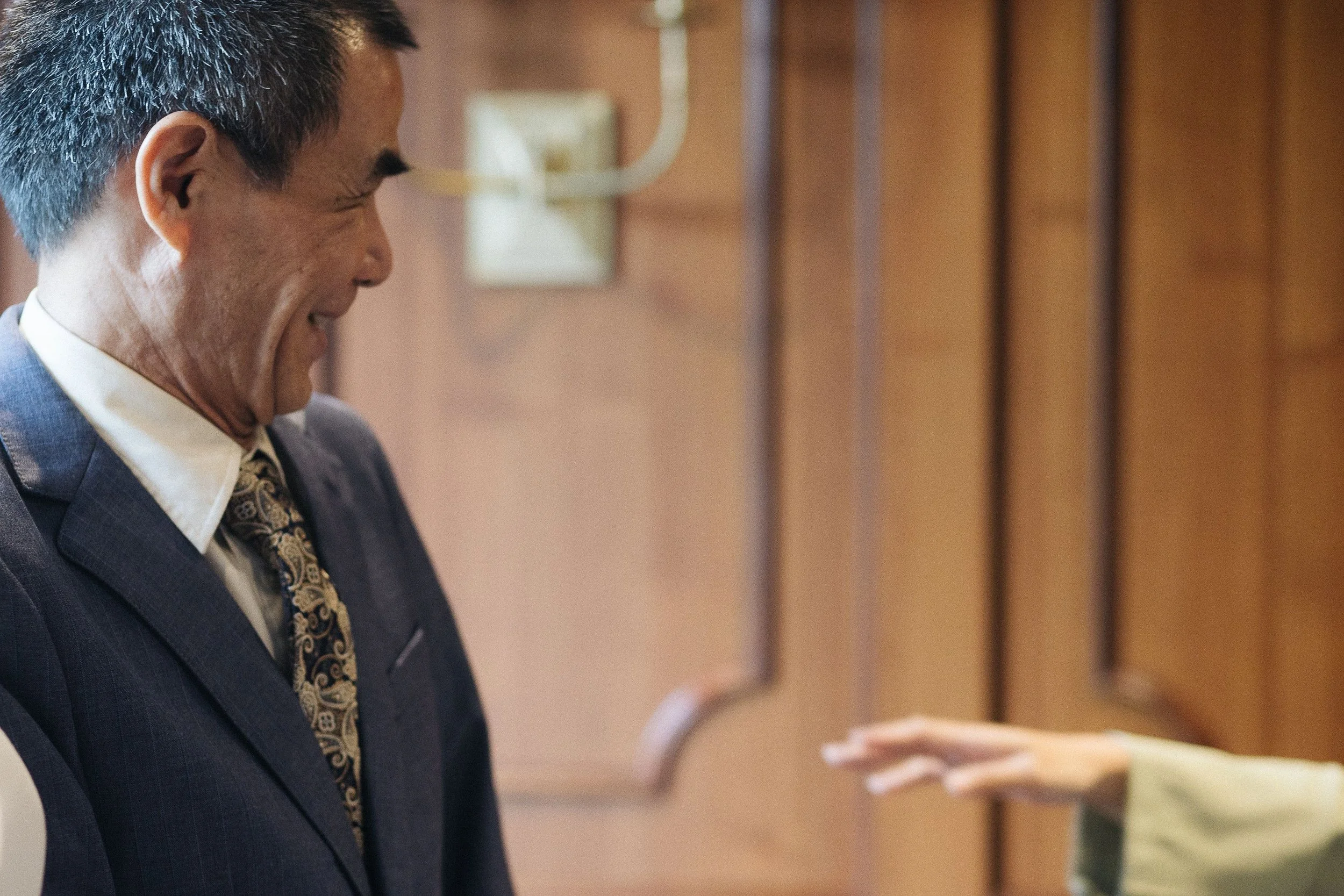 A man wearing a suit and tie, smiling as he accepts a piece of paper from another person in a formal setting.