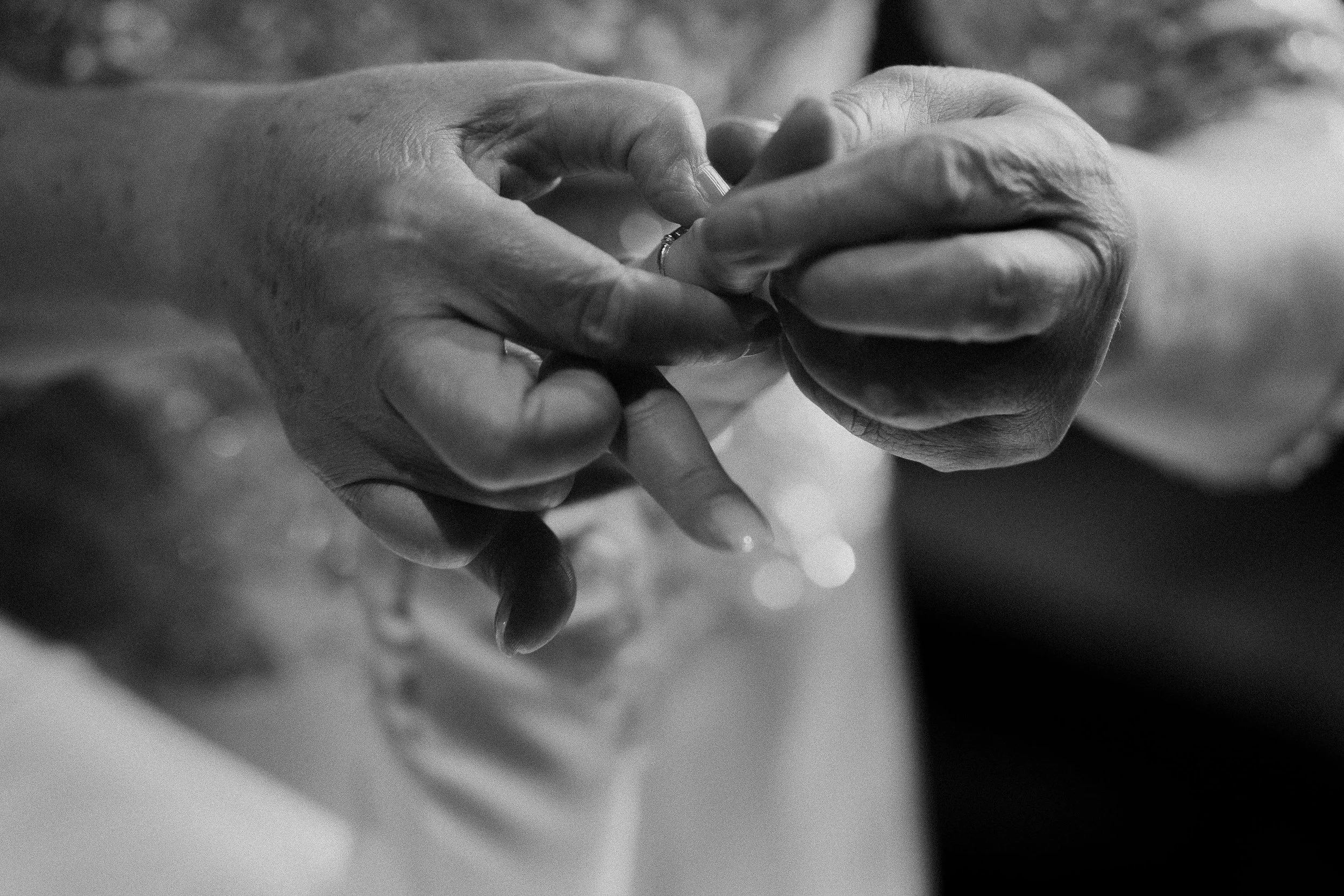 A close-up black and white photo of hands holding a small object, with a background of soft bokeh lights.