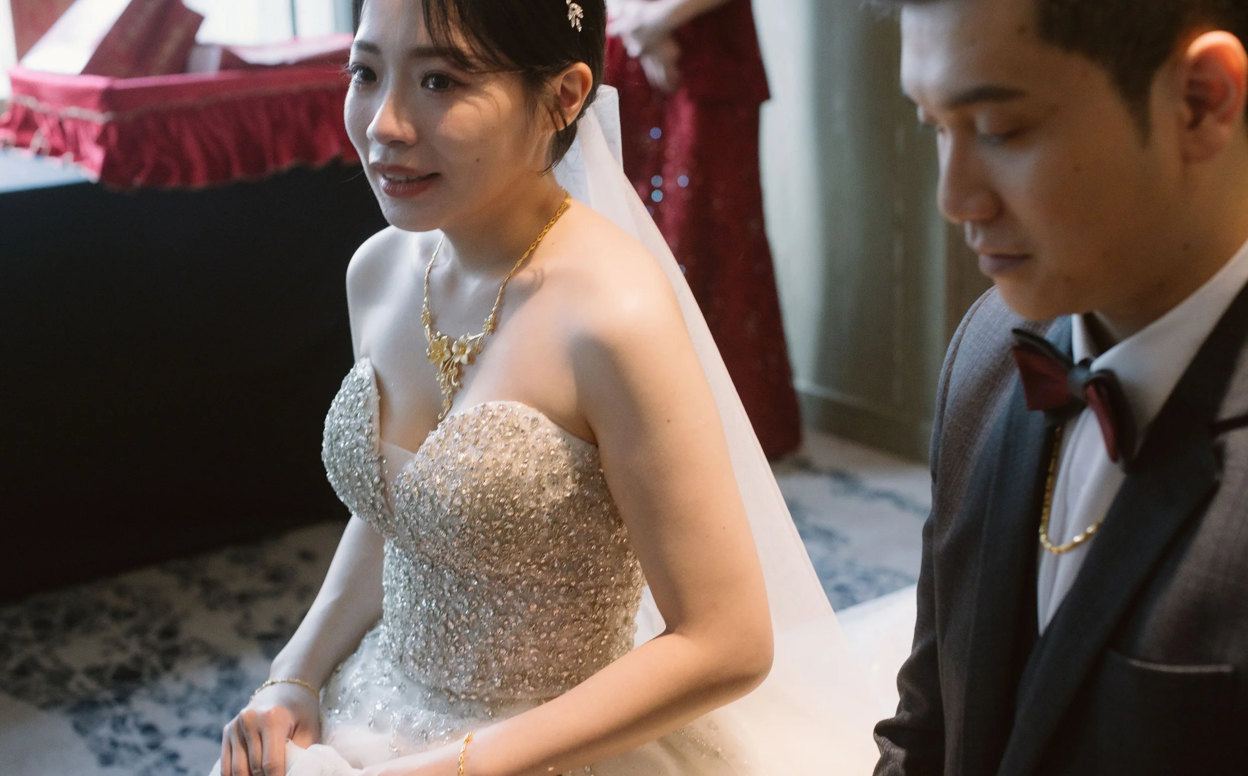 A bride and groom sitting together, dressed in wedding attire, in an indoor setting.