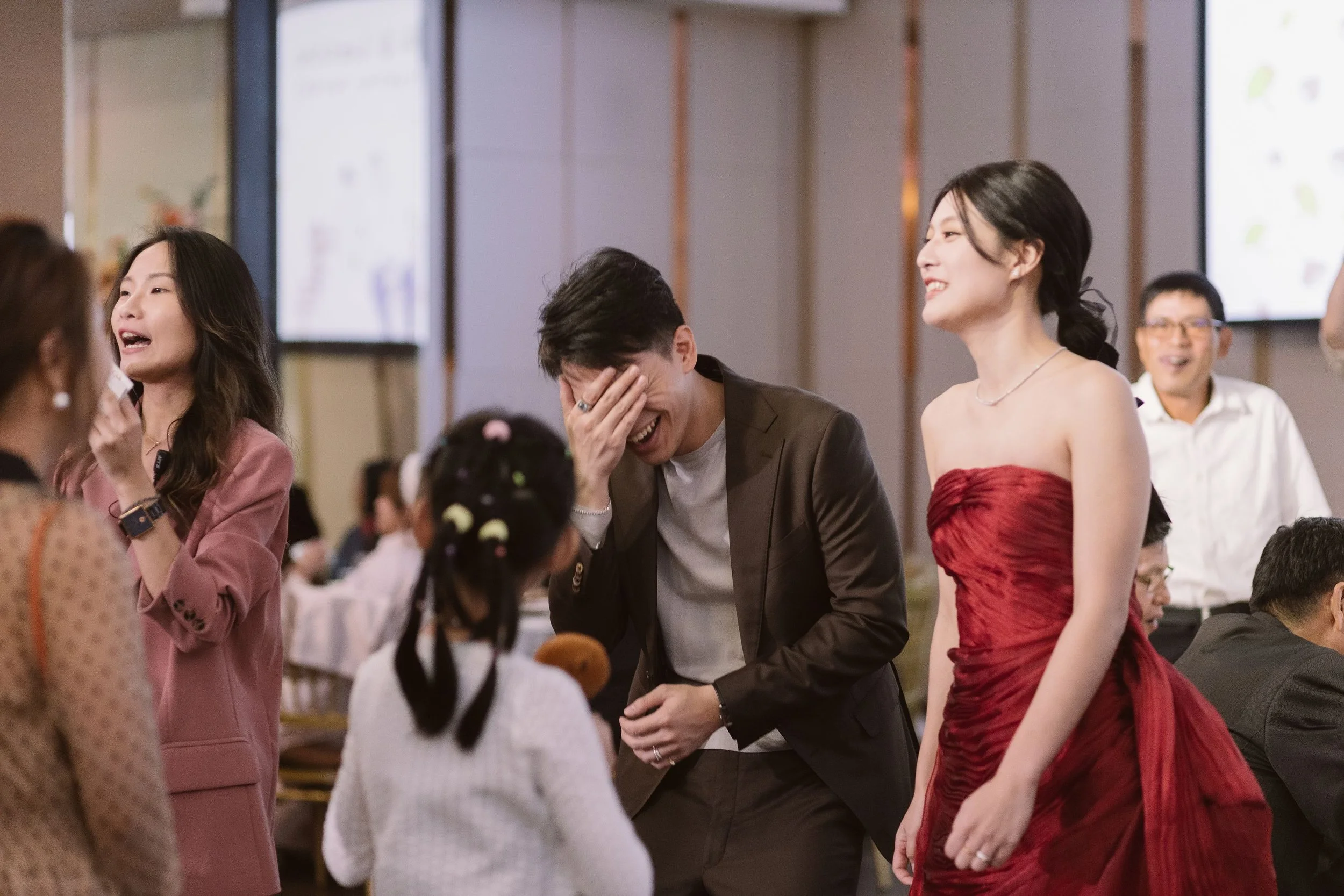 Group of people, including two women and a man, laughing and smiling at a social event in a decorated hall.