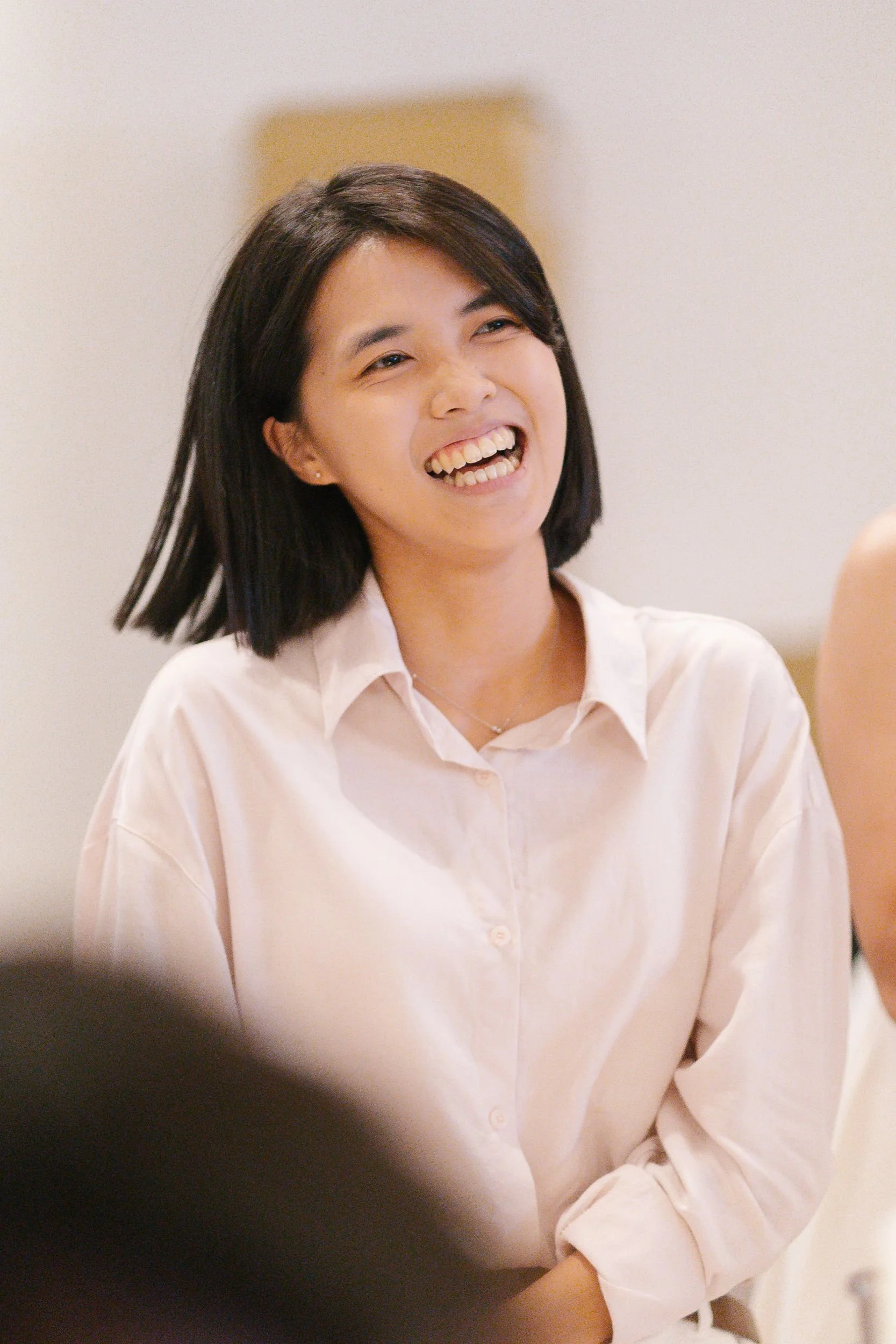 A woman with shoulder-length dark hair smiling and talking, wearing a light-colored shirt.
