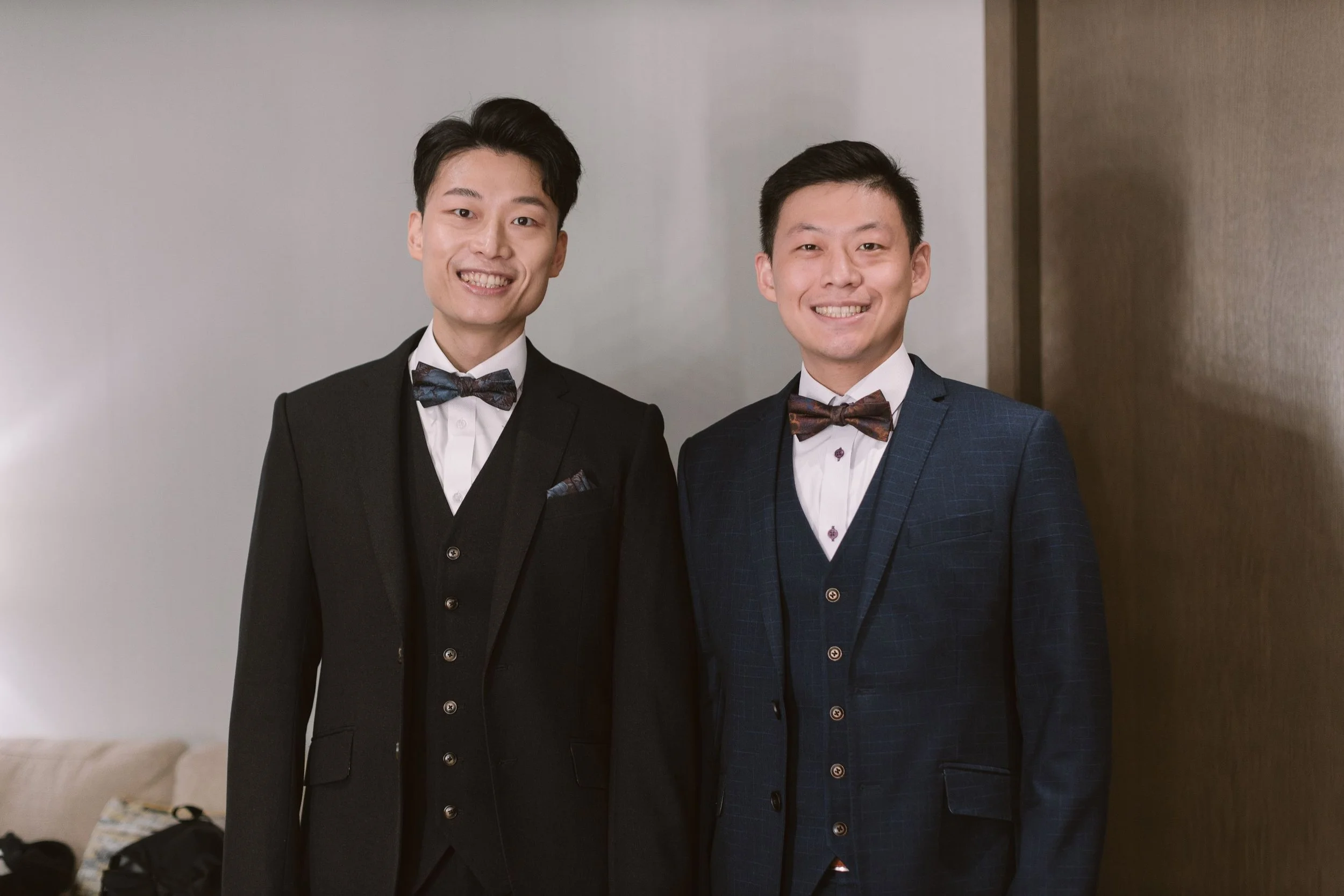 Two men dressed in tuxedos with bow ties, standing side by side and smiling at the camera.