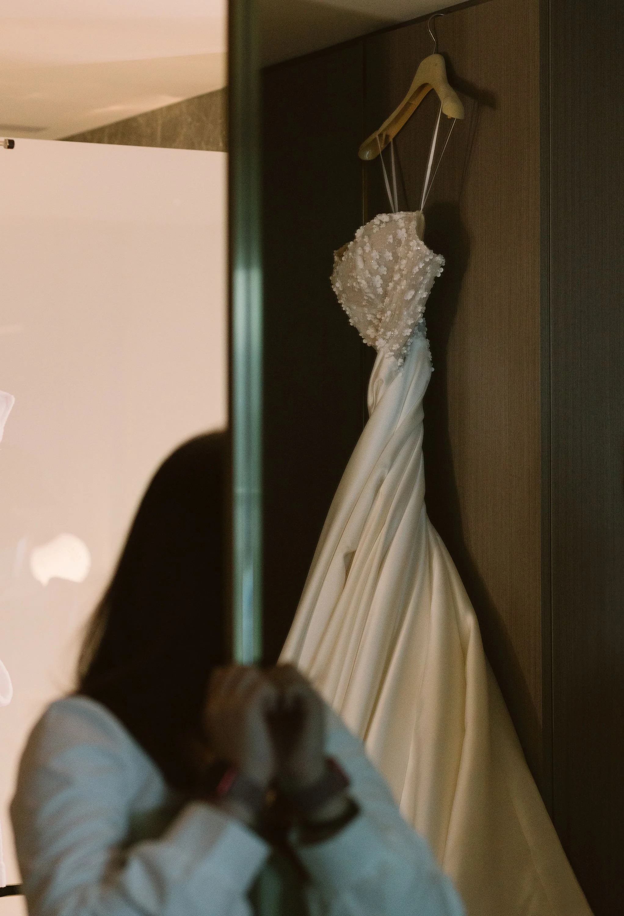 Empty wedding dress hanging on a wooden hanger inside a wardrobe.