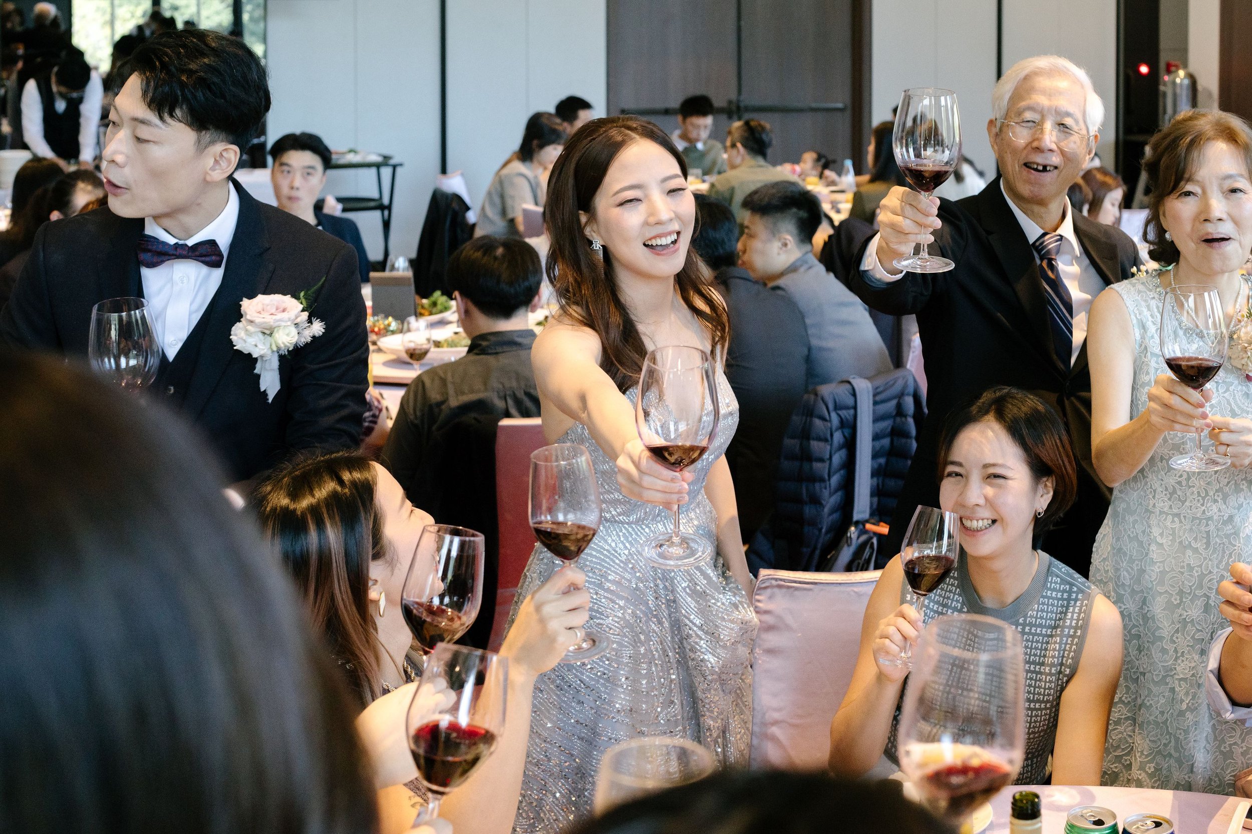 People at a celebratory event holding glasses of red wine, smiling and enjoying themselves.