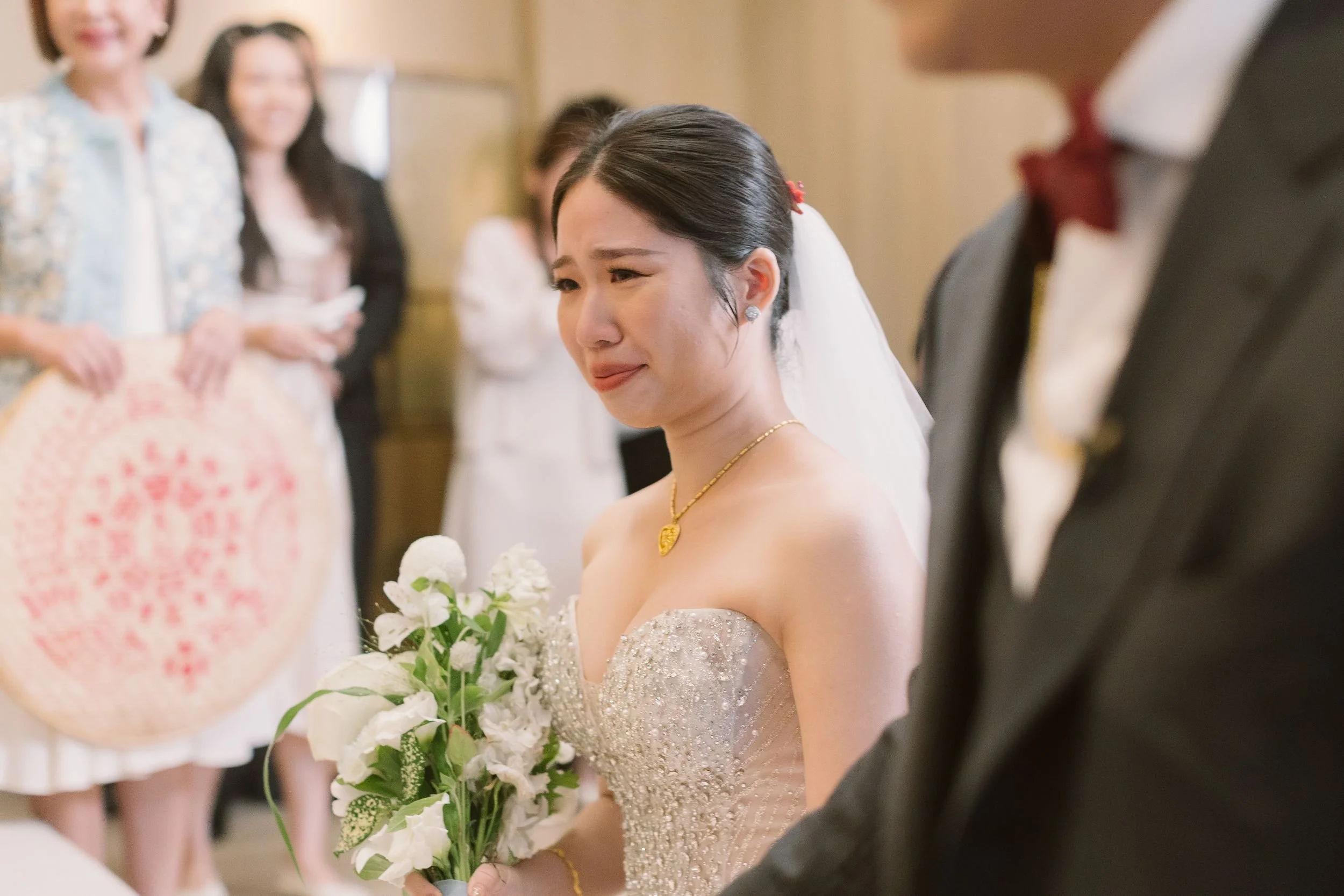 A bride in a wedding dress holding a bouquet of white flowers during her wedding ceremony, surrounded by guests.