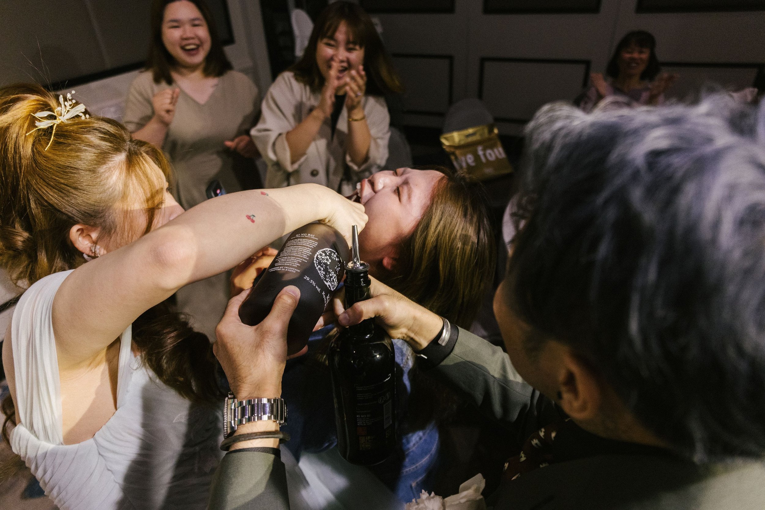 Group of women celebrating around a woman getting her nose pierced, surrounded by friends in an indoor space.