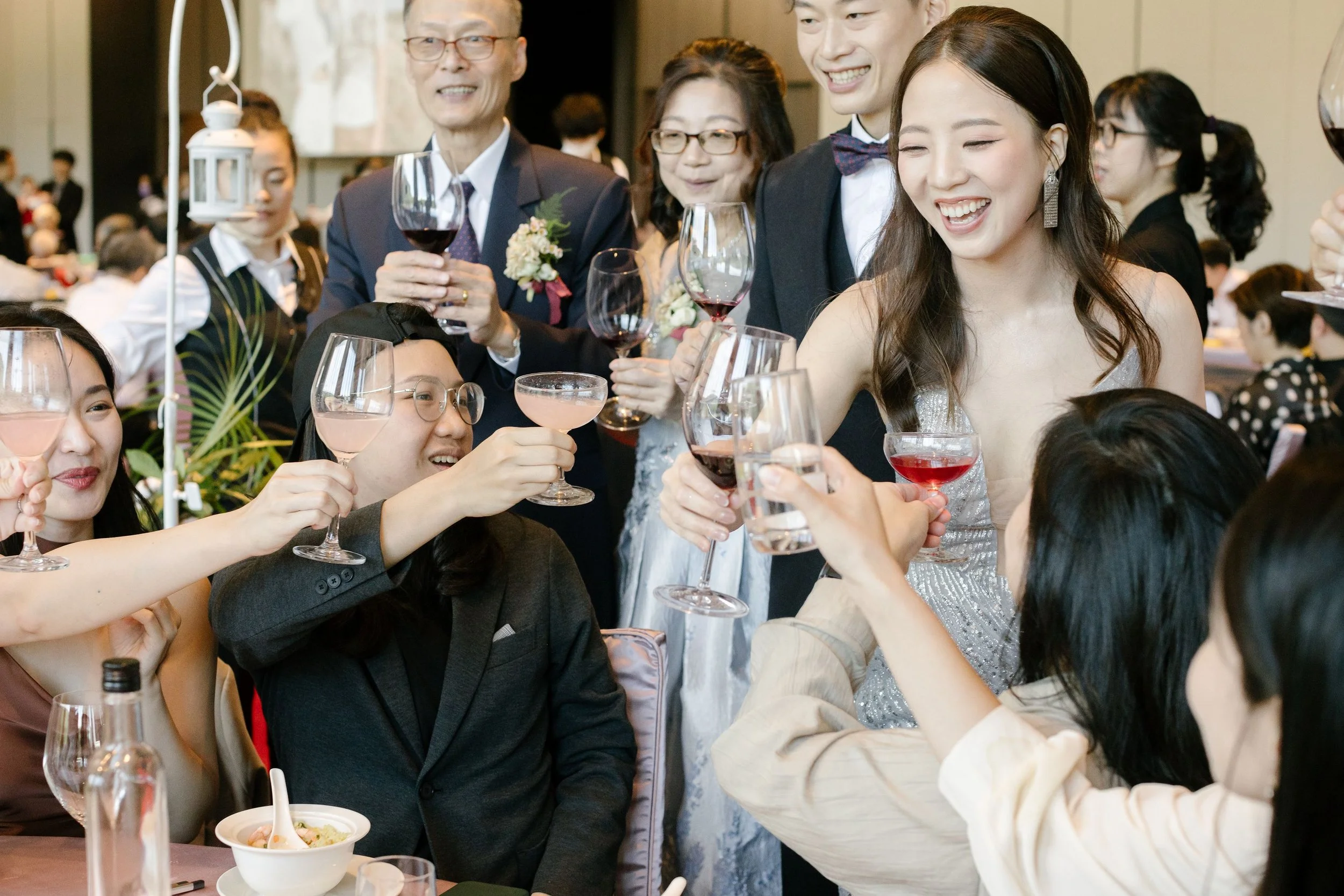 Group of diverse people in formal attire at a celebration raising glasses of wine and toast together, smiling and enjoying a festive gathering.