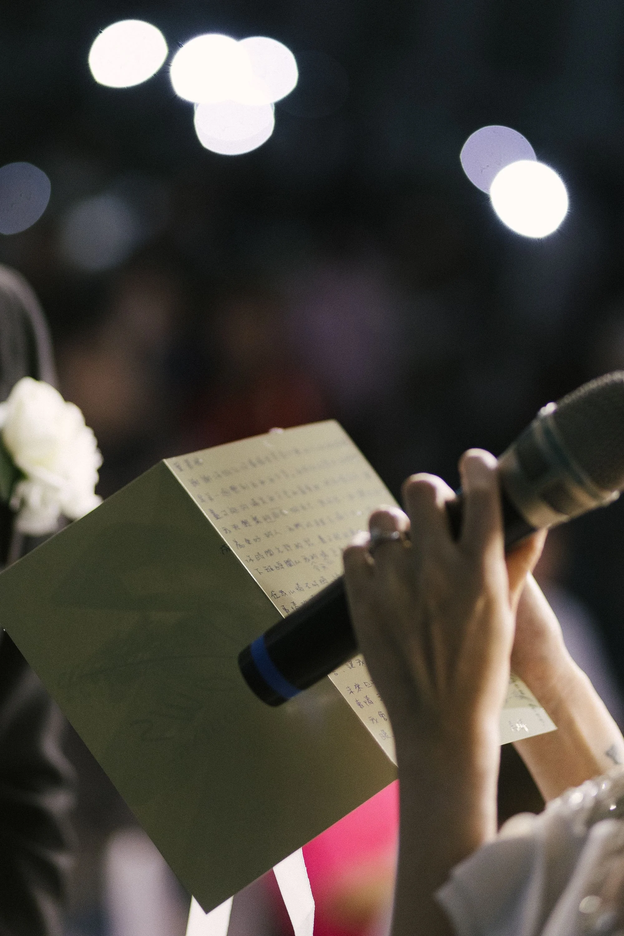 A person holding a black marker and a small notebook with handwritten notes, with a blurred background of bright circular lights.
