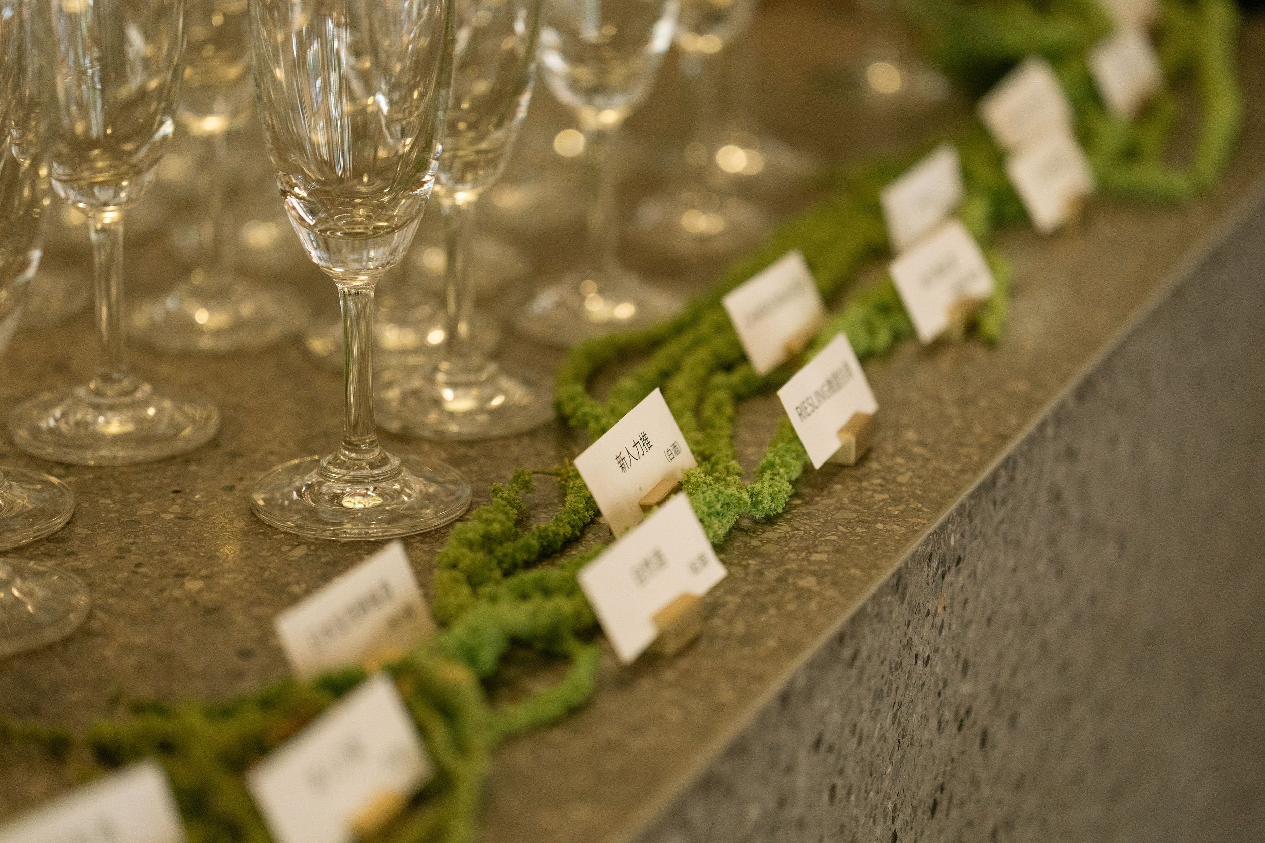 Several empty champagne flutes lined up on a table with small labels and green decorations nearby.
