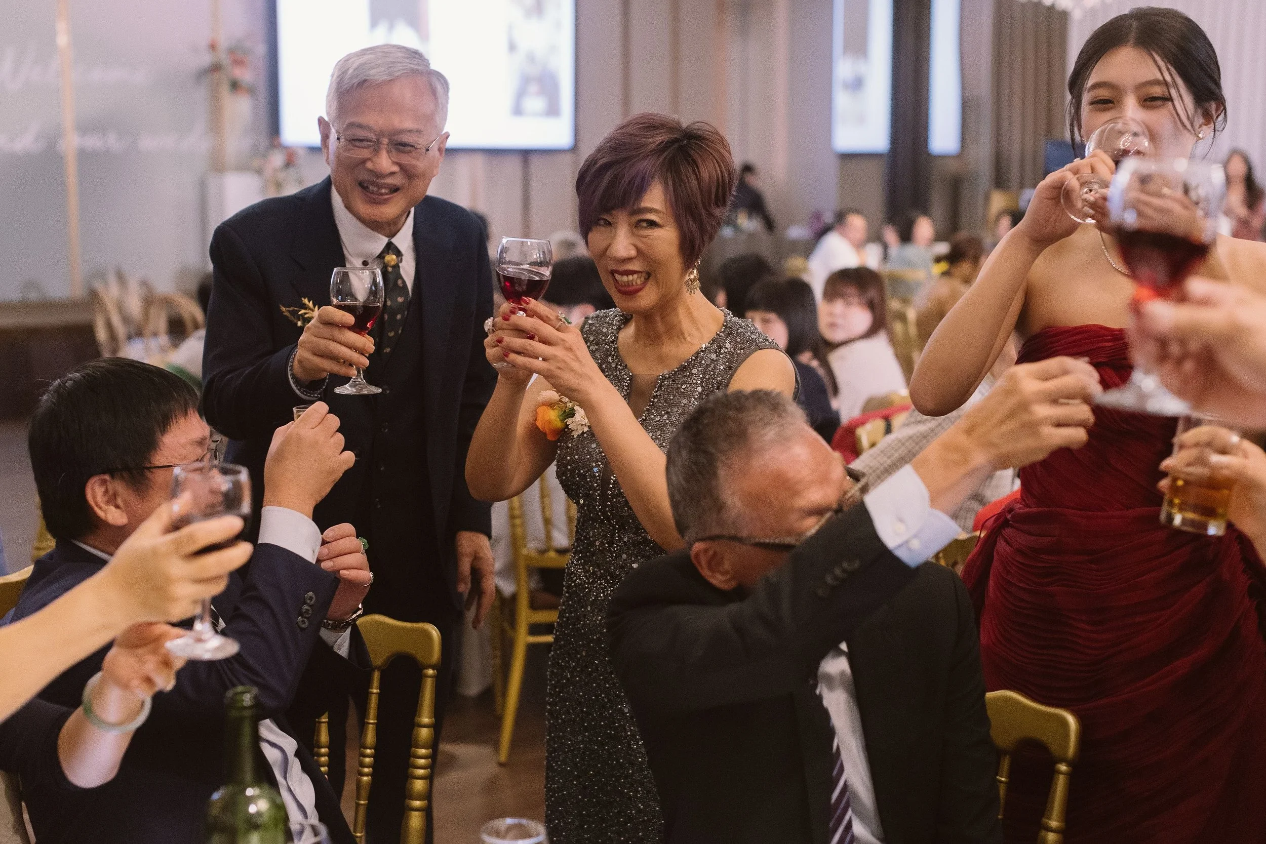 People at a formal gathering raising glasses of red wine and smiling.