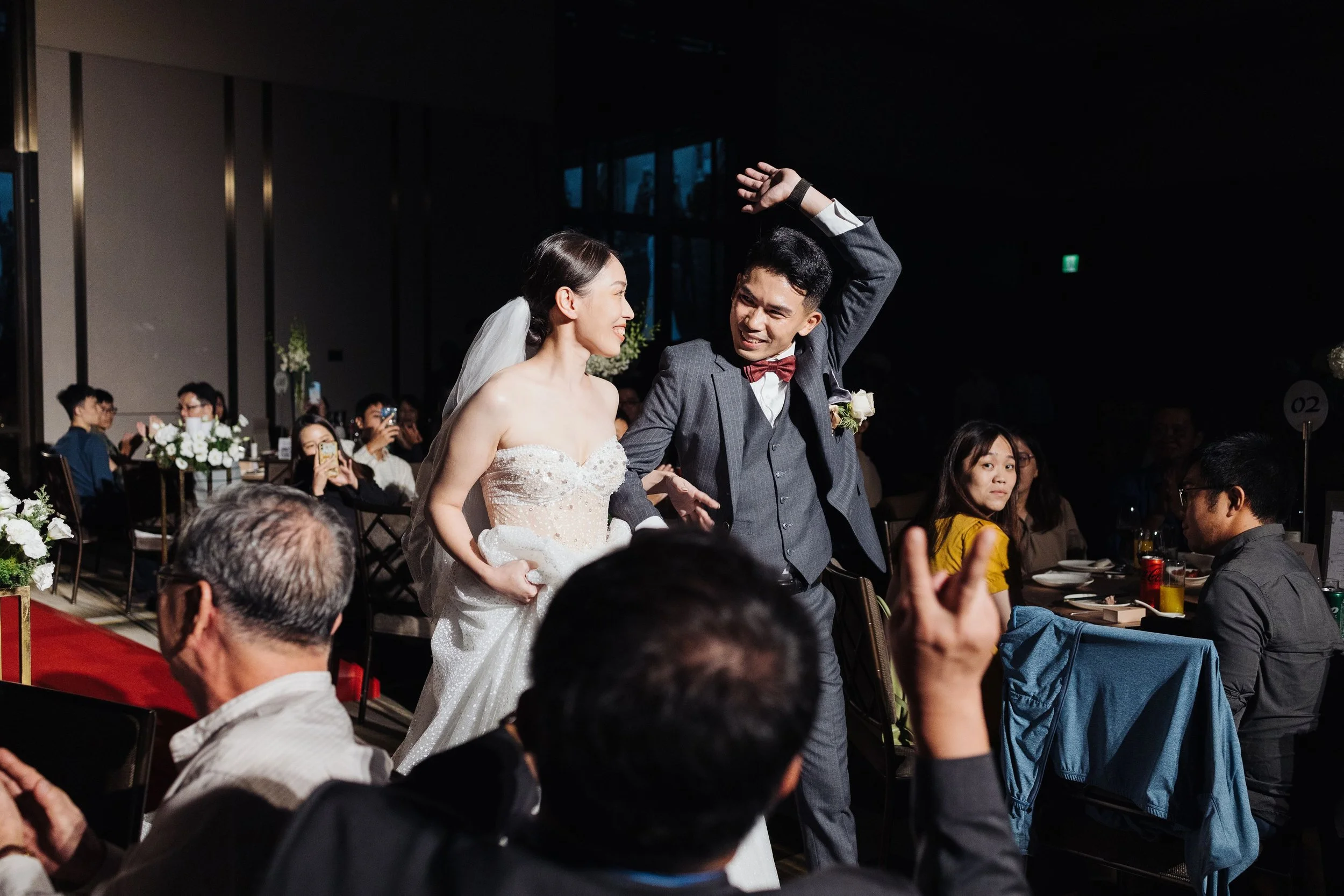 A bride and groom dancing at their wedding reception, surrounded by seated guests in a decorated indoor venue.