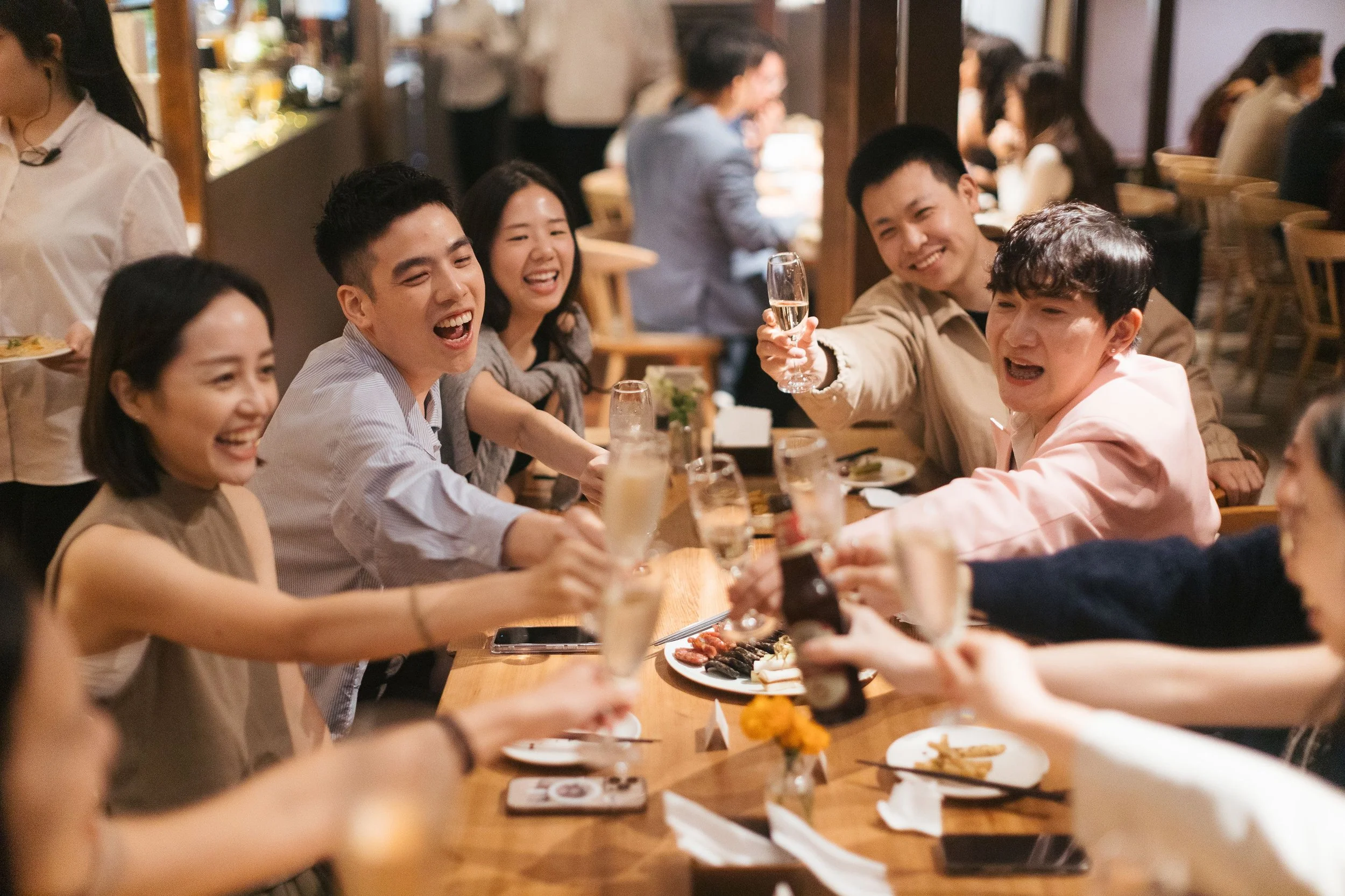 A group of friends enjoying a meal together at a restaurant, smiling and raising glasses in a toast.