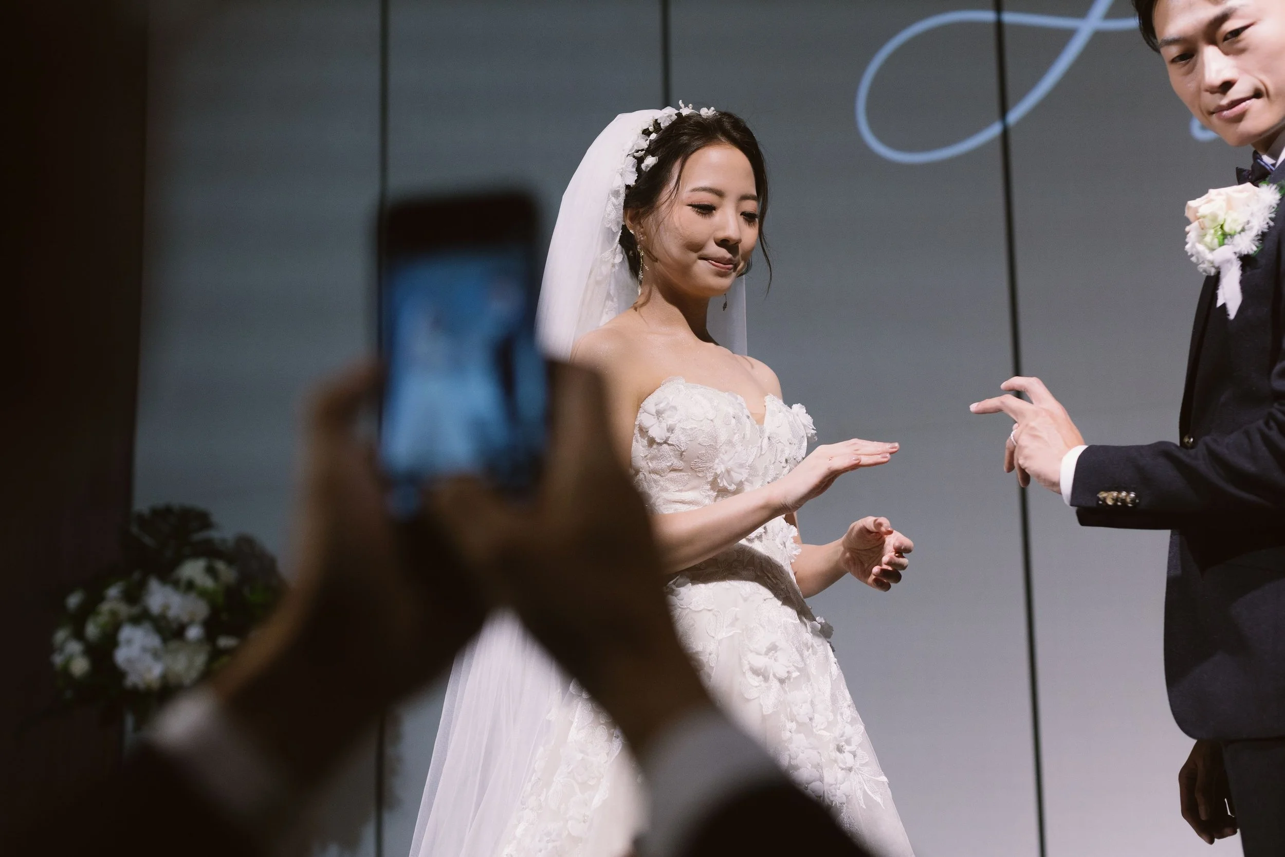 A bride and groom at their wedding, with a person taking a photo of them in the foreground.