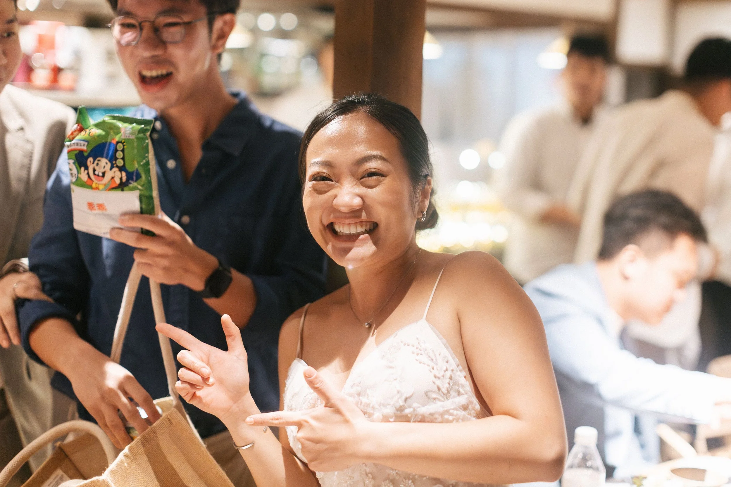 Two people smiling and enjoying themselves at a social gathering, one holding a bag of snacks and both making playful gestures.