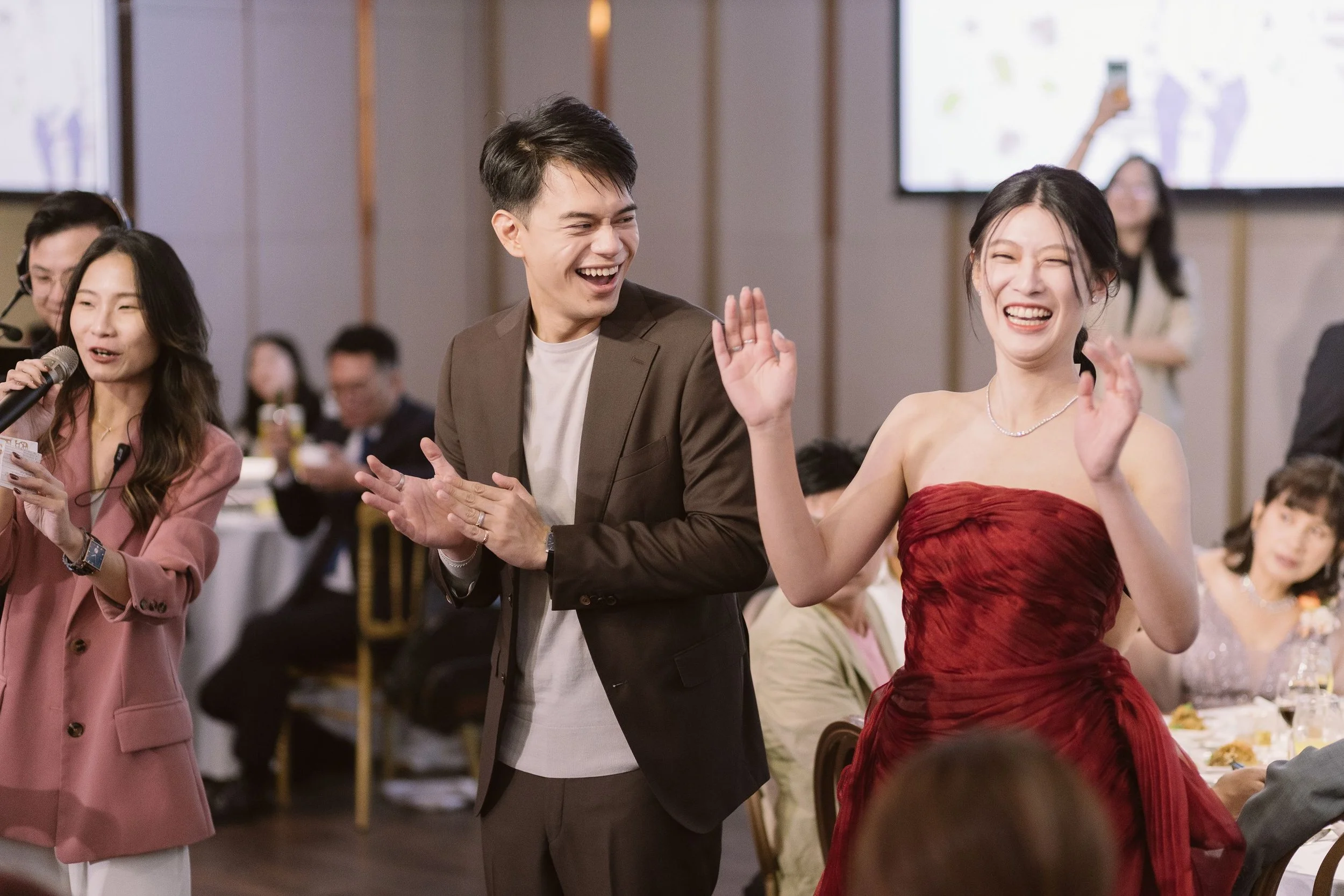 People at a celebratory event, smiling and clapping, with a woman in a red dress in the foreground.