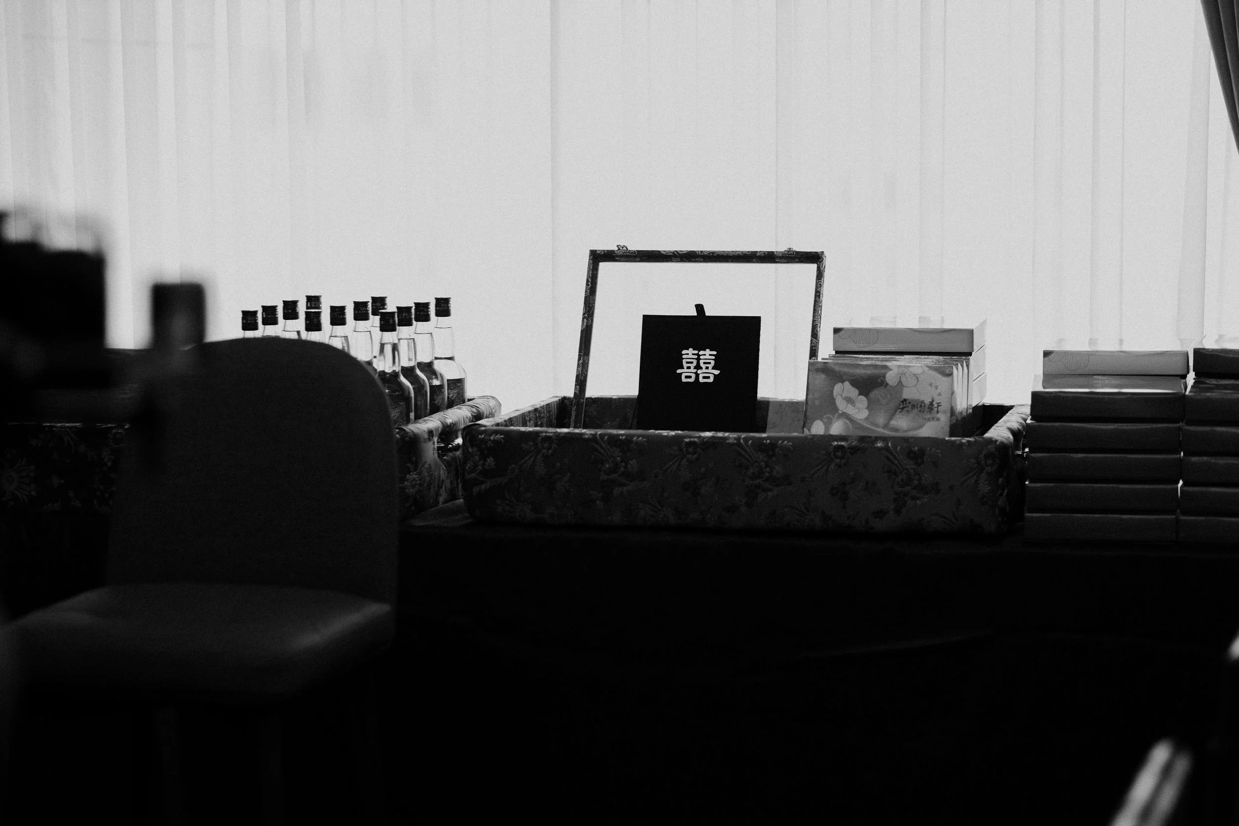 A black and white image showing a table with bottles, a framed picture with Chinese characters, and some boxes.