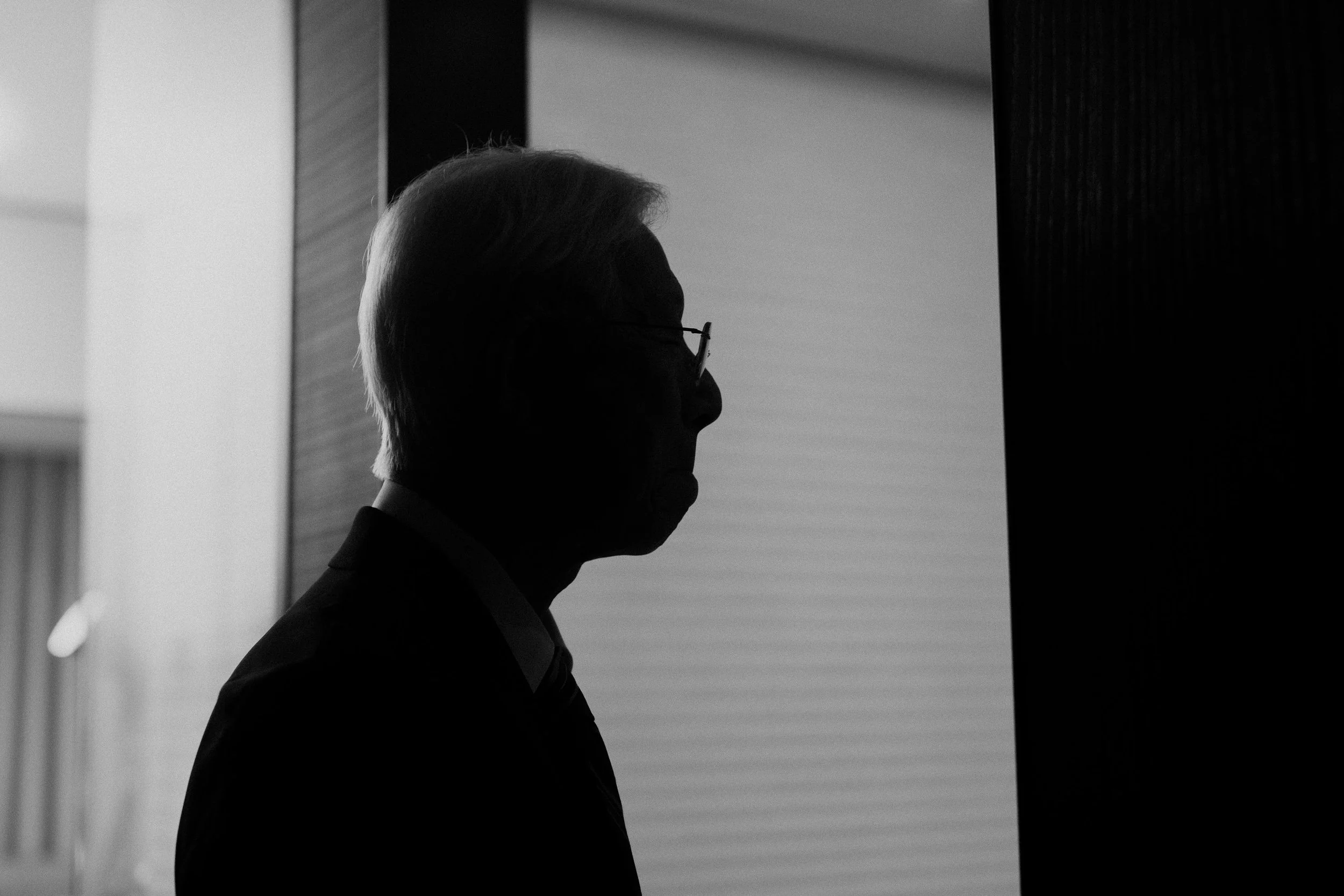 Silhouette of a man with glasses, possibly in profile, standing indoors near a window or light source.