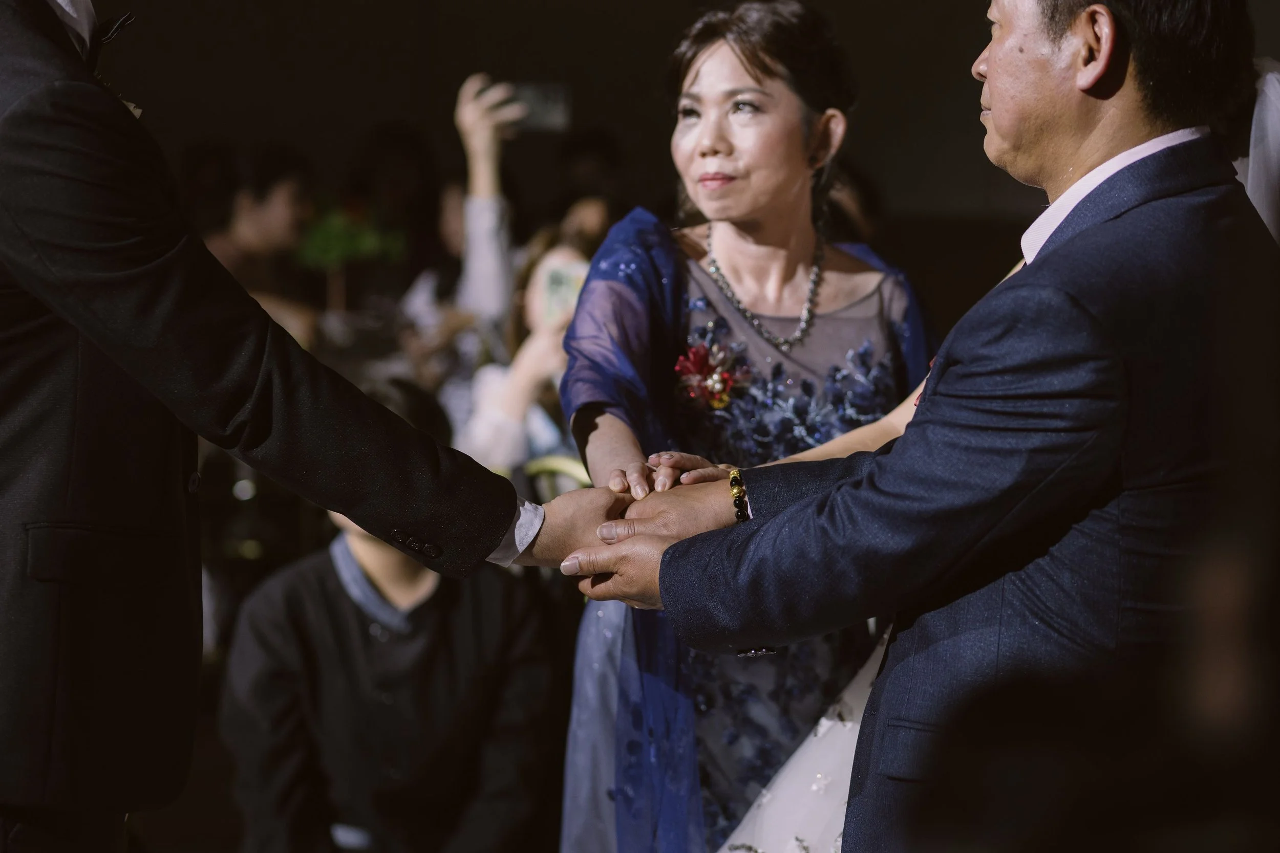 A woman in a blue dress and two men in suits holding hands during a wedding or formal event.