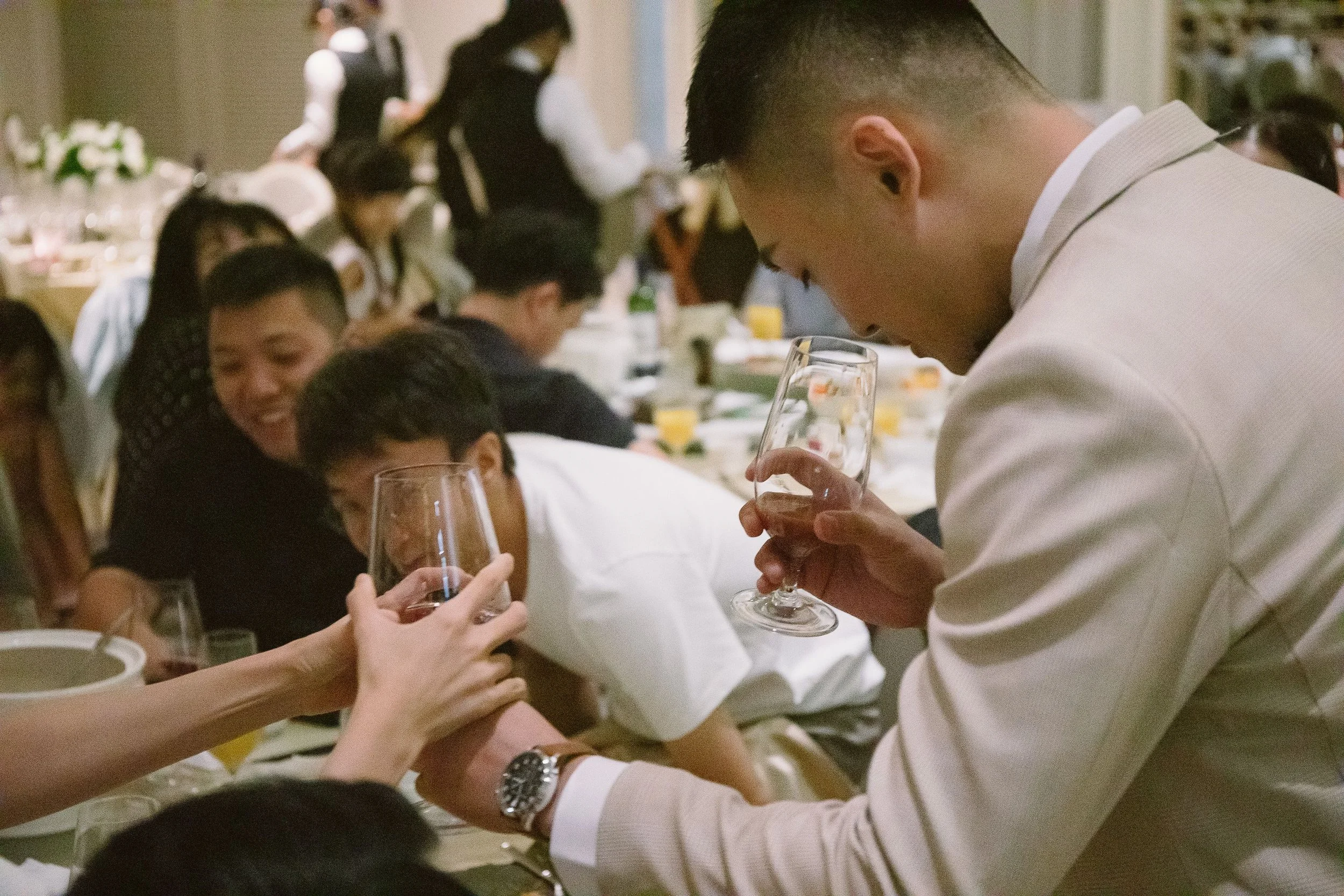 People at a dinner table holding wine glasses, some smiling and toasting each other.