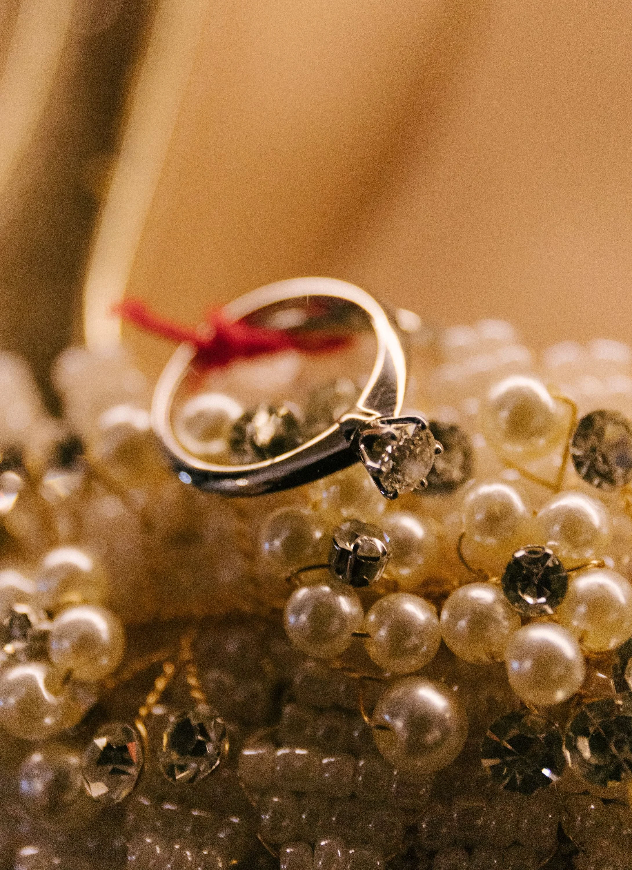 Close-up of a pearl necklace with a silver ring, purple gemstone earrings, and a hairpin with a pearl and diamond embellishment, arranged on a reflective surface.