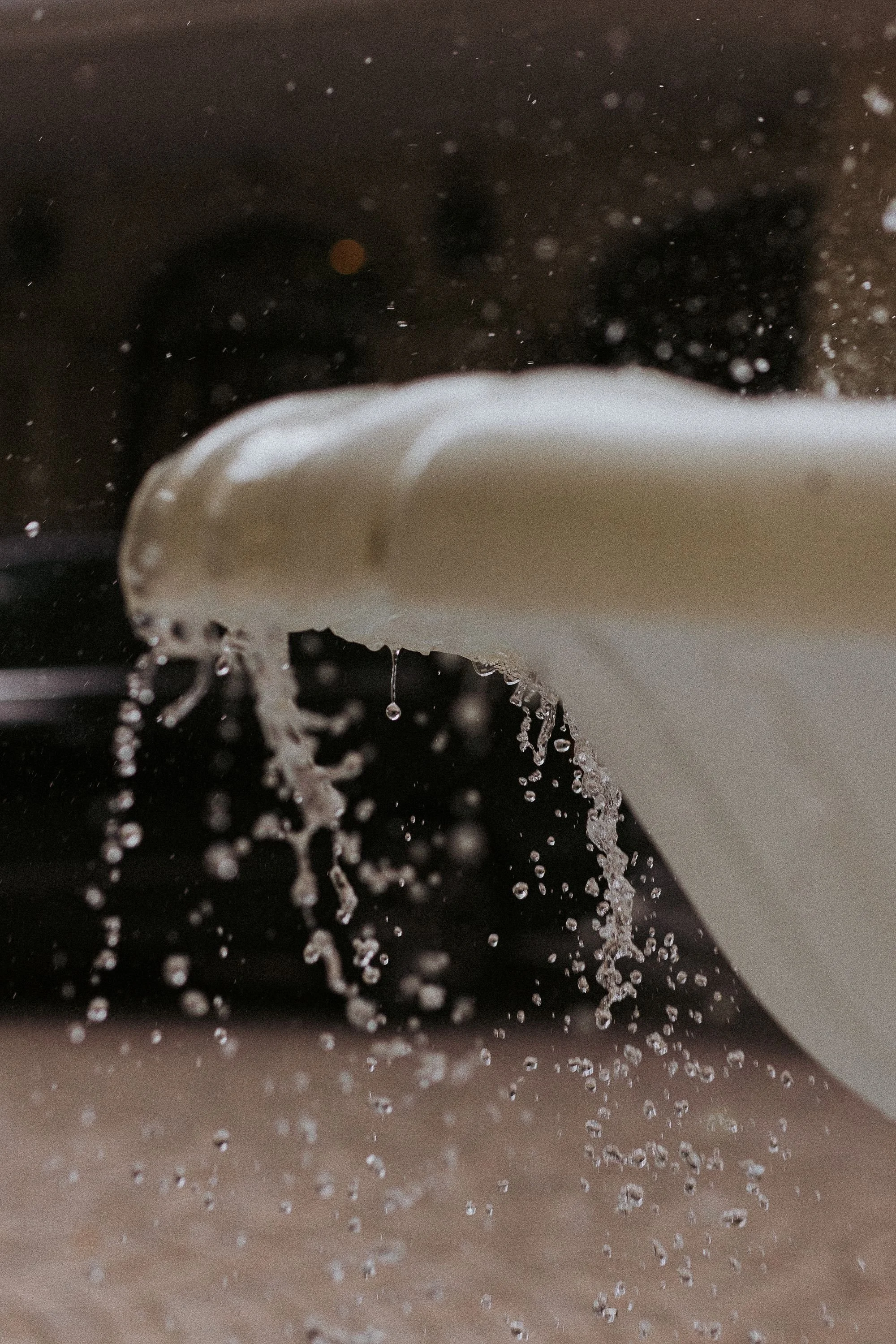 Close-up of a mug overflowing with milk, spilling over onto a dark surface above a wooden table.