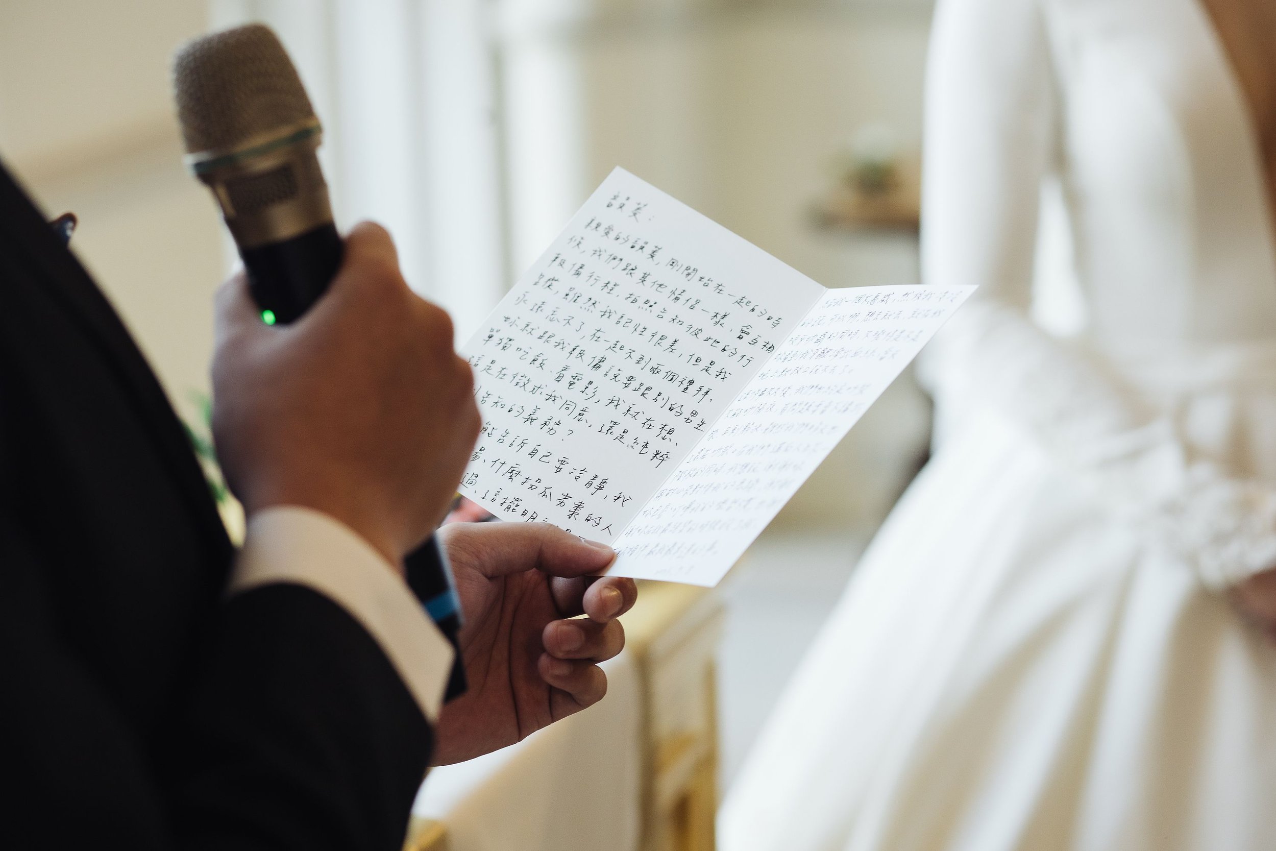 A person holding a microphone in one hand and reading from a handwritten letter in Chinese characters.