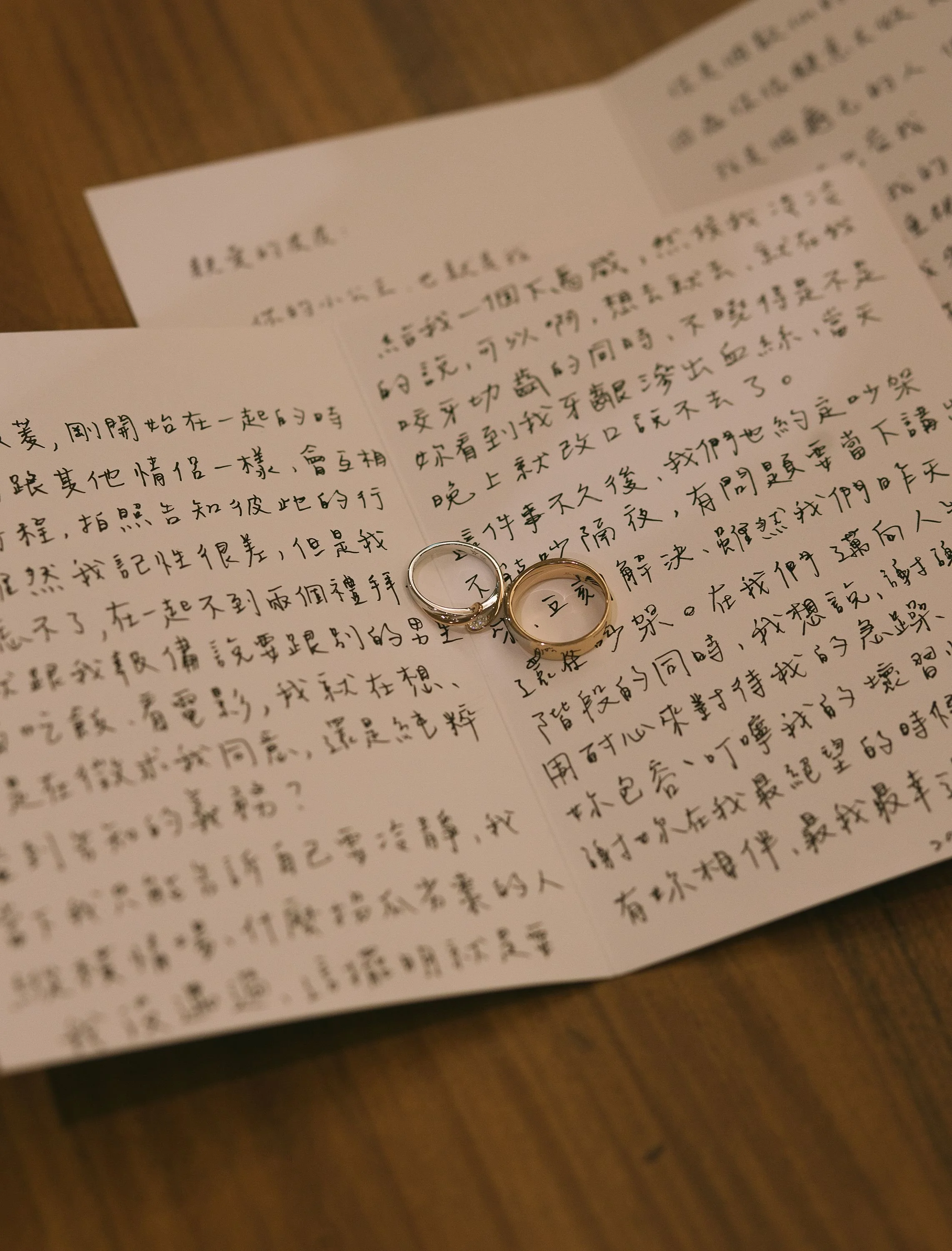 Two wedding rings resting on a handwritten letter in Chinese characters, on a wooden surface.